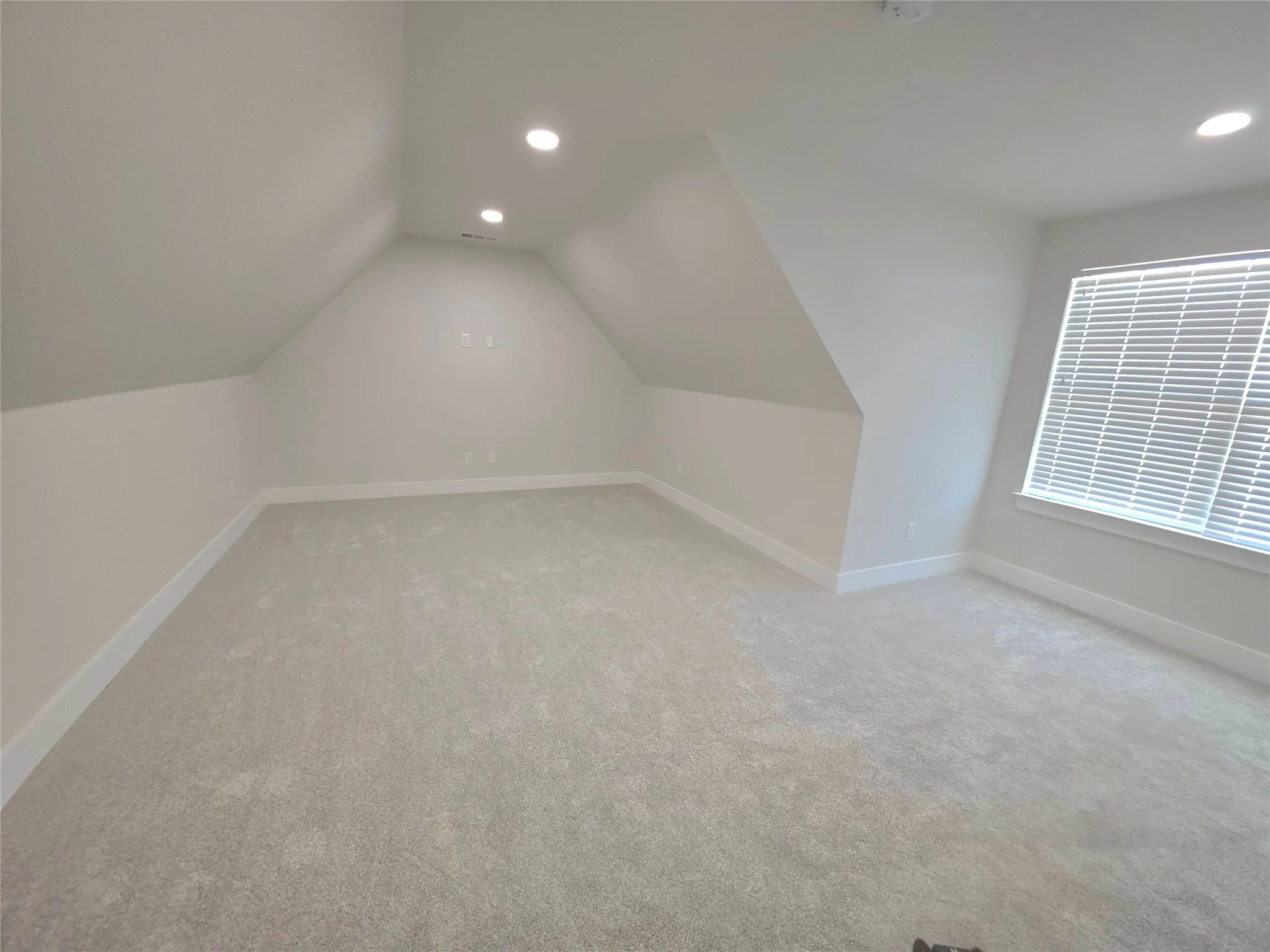 Finished interior space featuring vaulted ceilings, neutral wall tones, wall-to-wall carpeting, recessed lighting, and horizontal window blinds