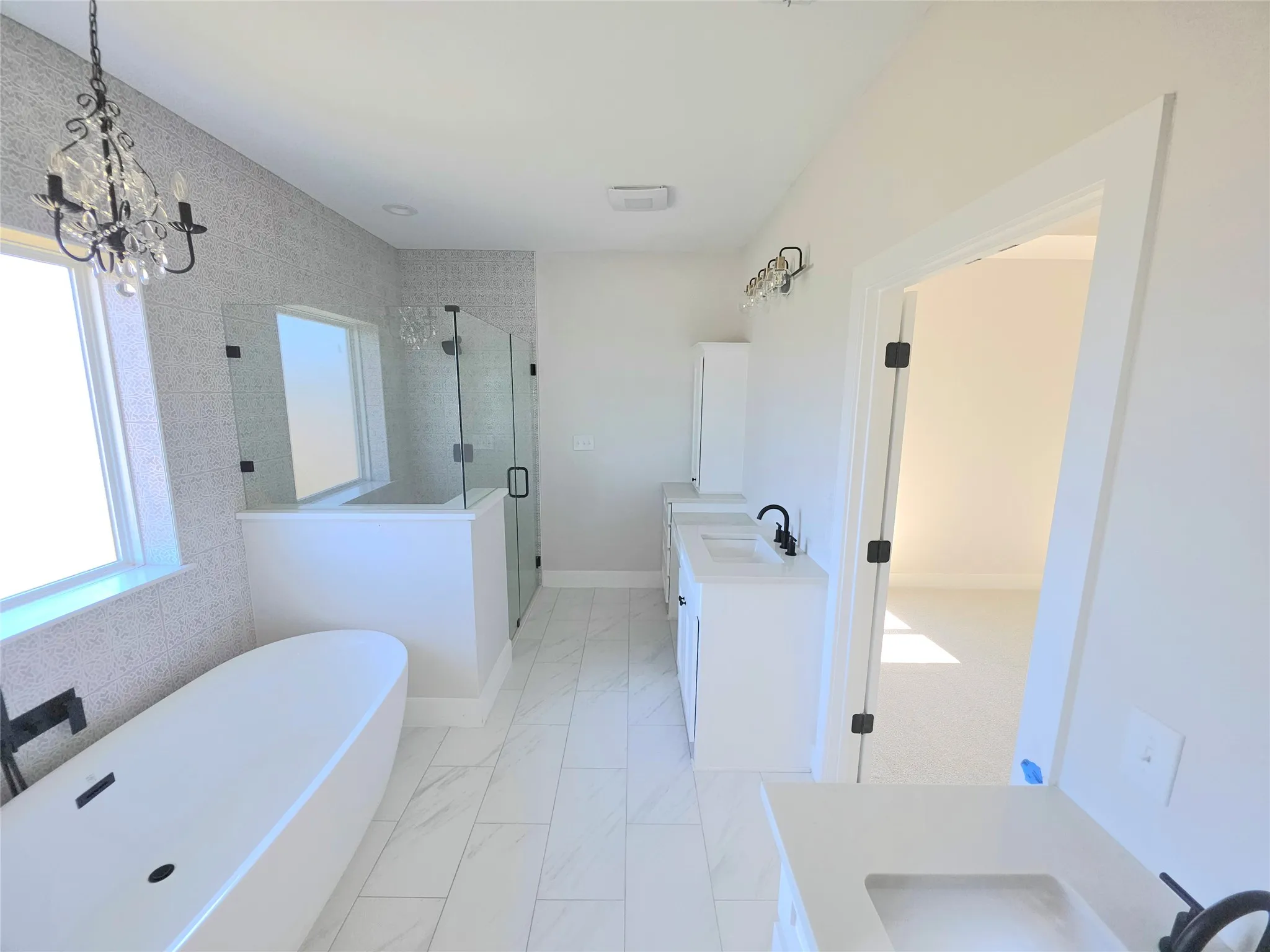 Freestanding soaking tub with a wall-mounted faucet, walk-in glass shower, dual white vanities with rectangular under-mount sinks, and large-format porcelain tile flooring