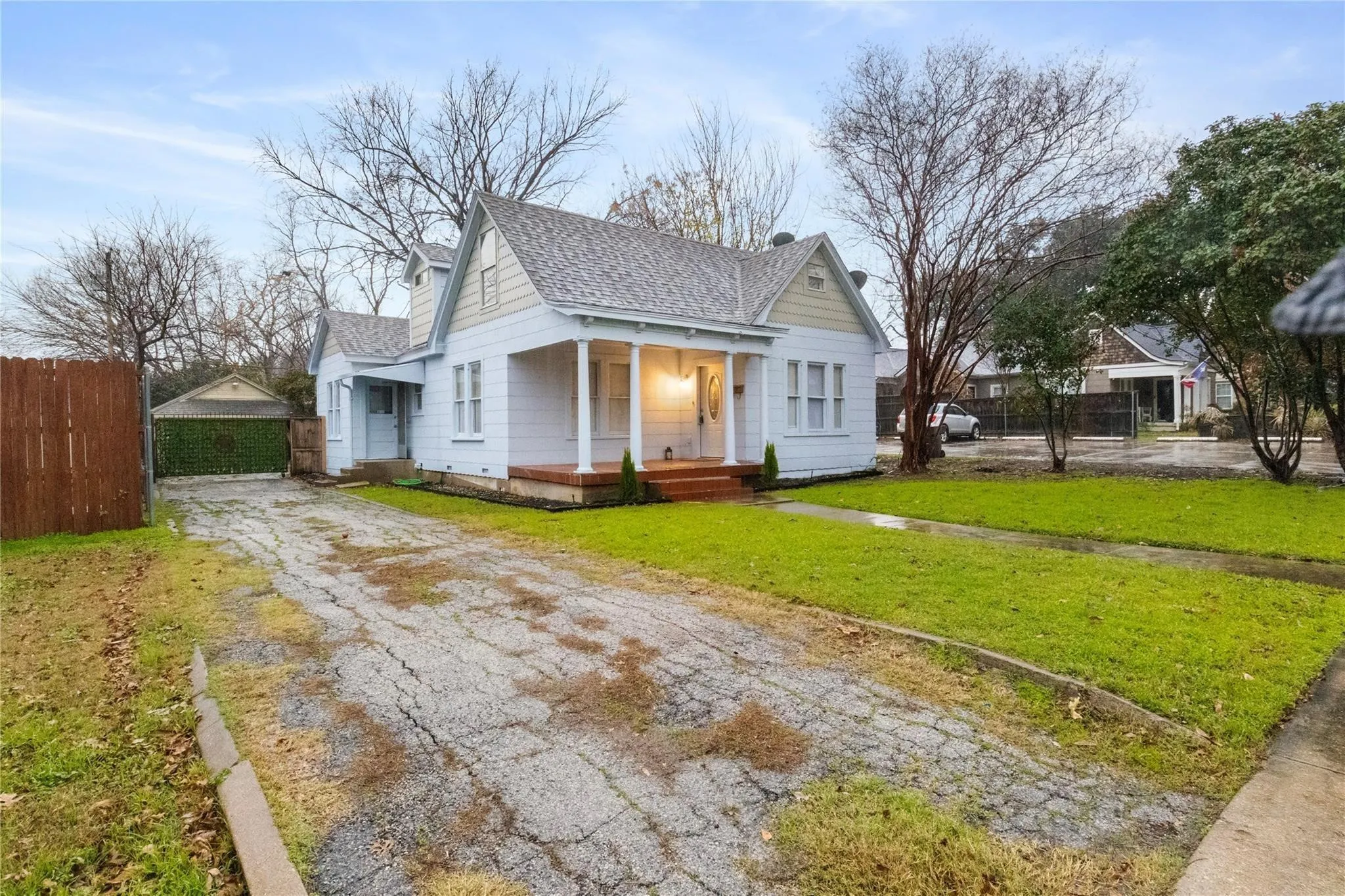 Exterior featuring light-toned siding, a covered front porch with classic columns, a steeply pitched roofline, and a detached structure