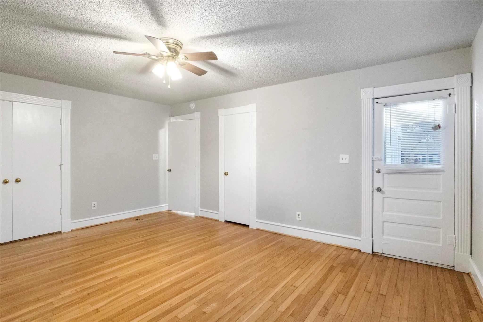 Hardwood flooring, ceiling-mounted light fixture with fan, and a solid-core door with glass inset