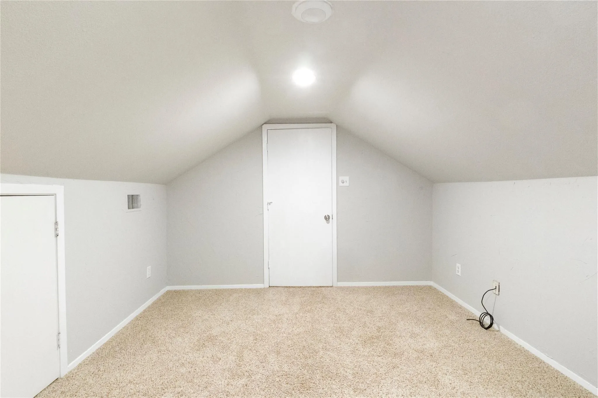 Finished attic space featuring vaulted ceilings, neutral carpeting, and integrated storage access doors