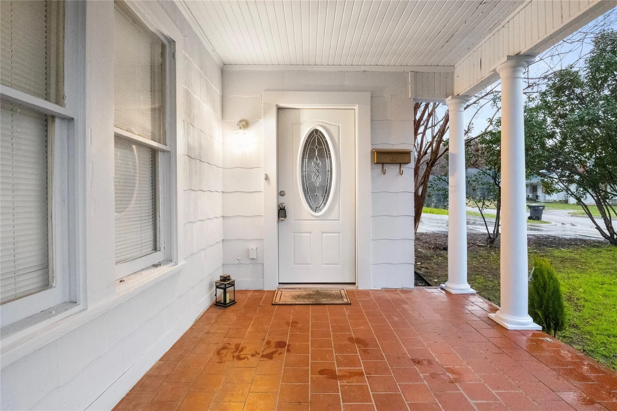 Covered porch featuring terracotta-style tile flooring, classic round columns, and a white front door with an oval glass insert