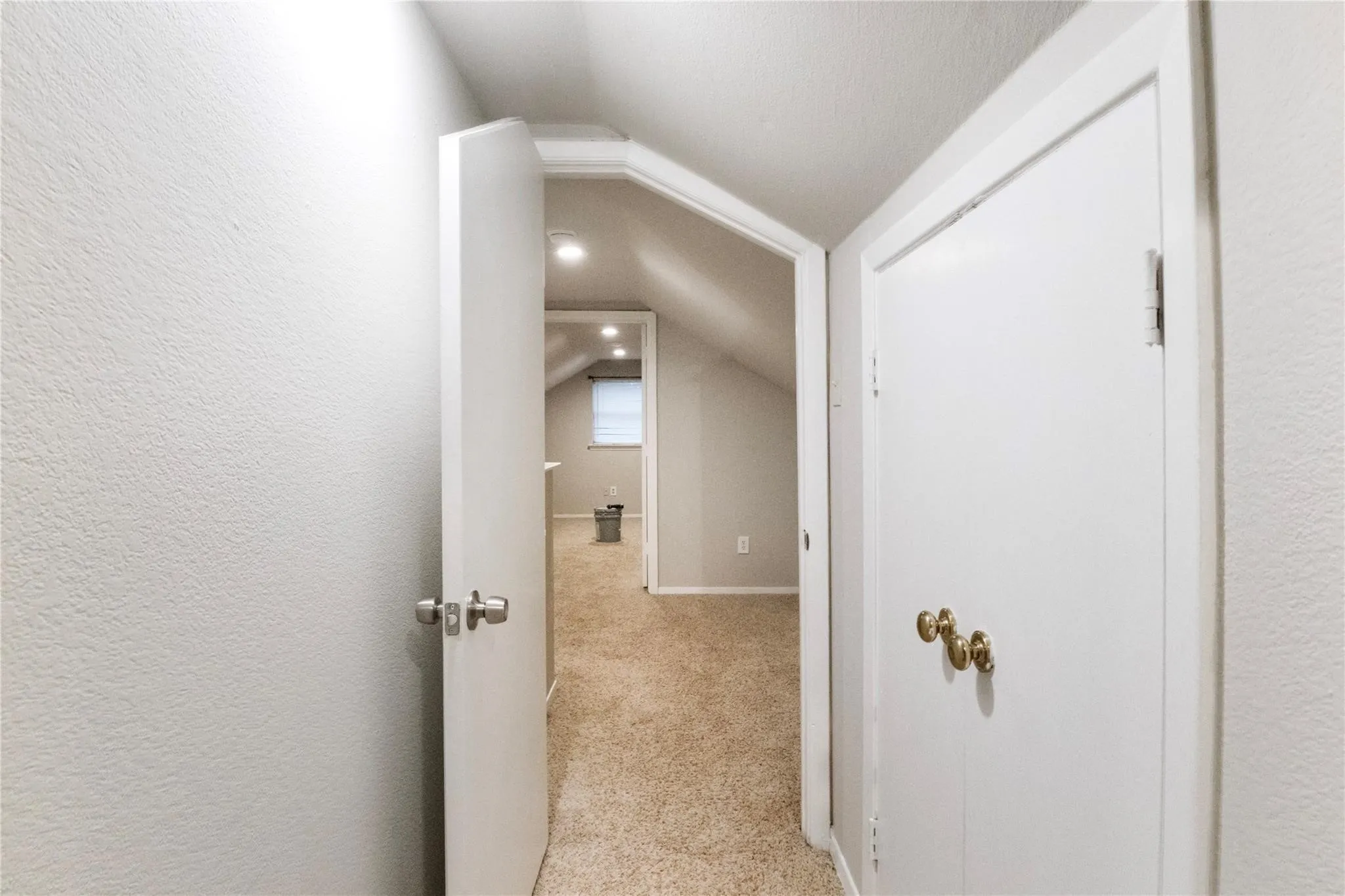 Sloped ceilings featuring neutral carpeting, recessed lighting, and white interior doors with metallic hardware