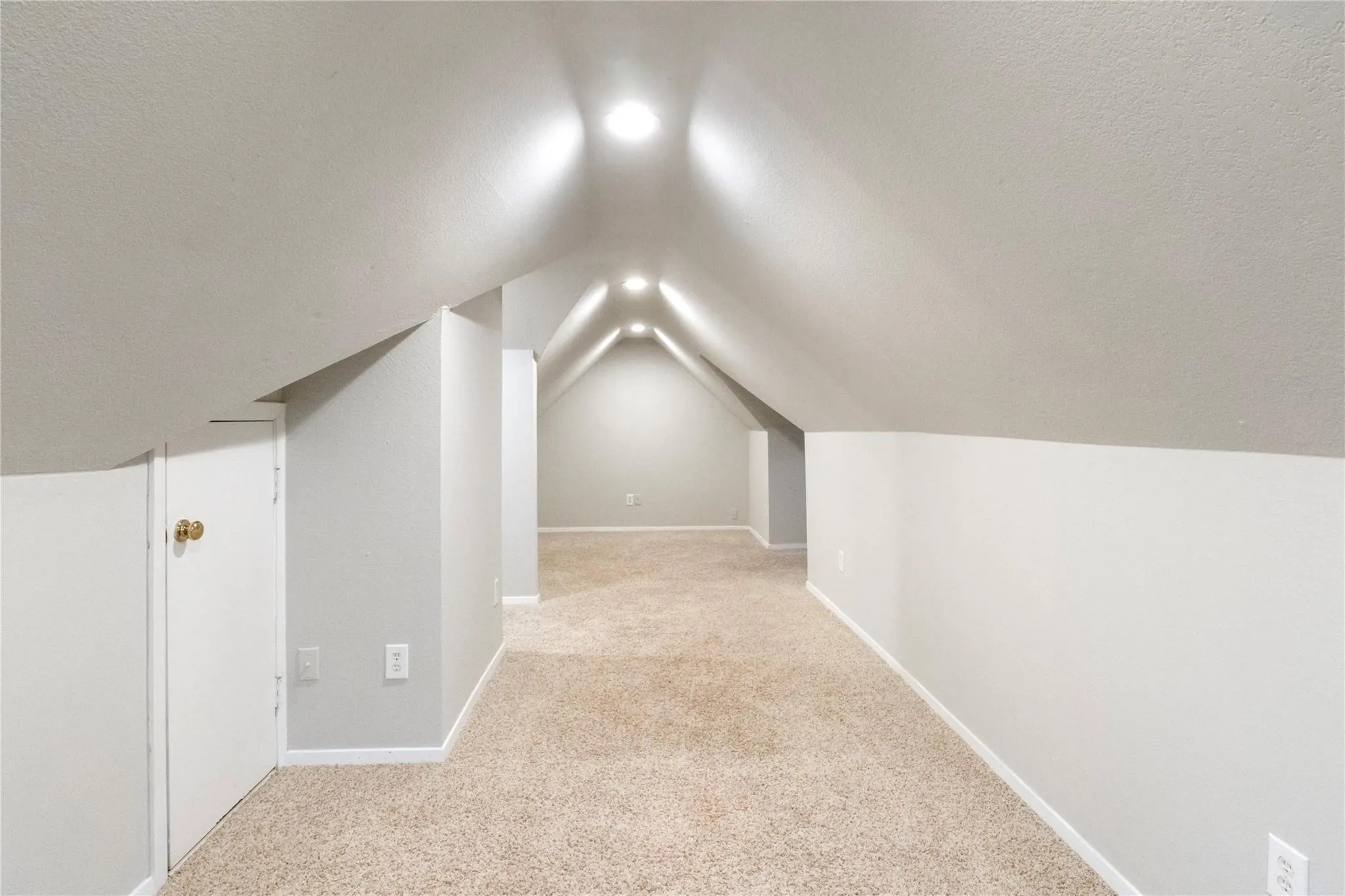 Finished attic space featuring vaulted ceilings, neutral carpeting, recessed lighting, and integrated knee-wall storage access