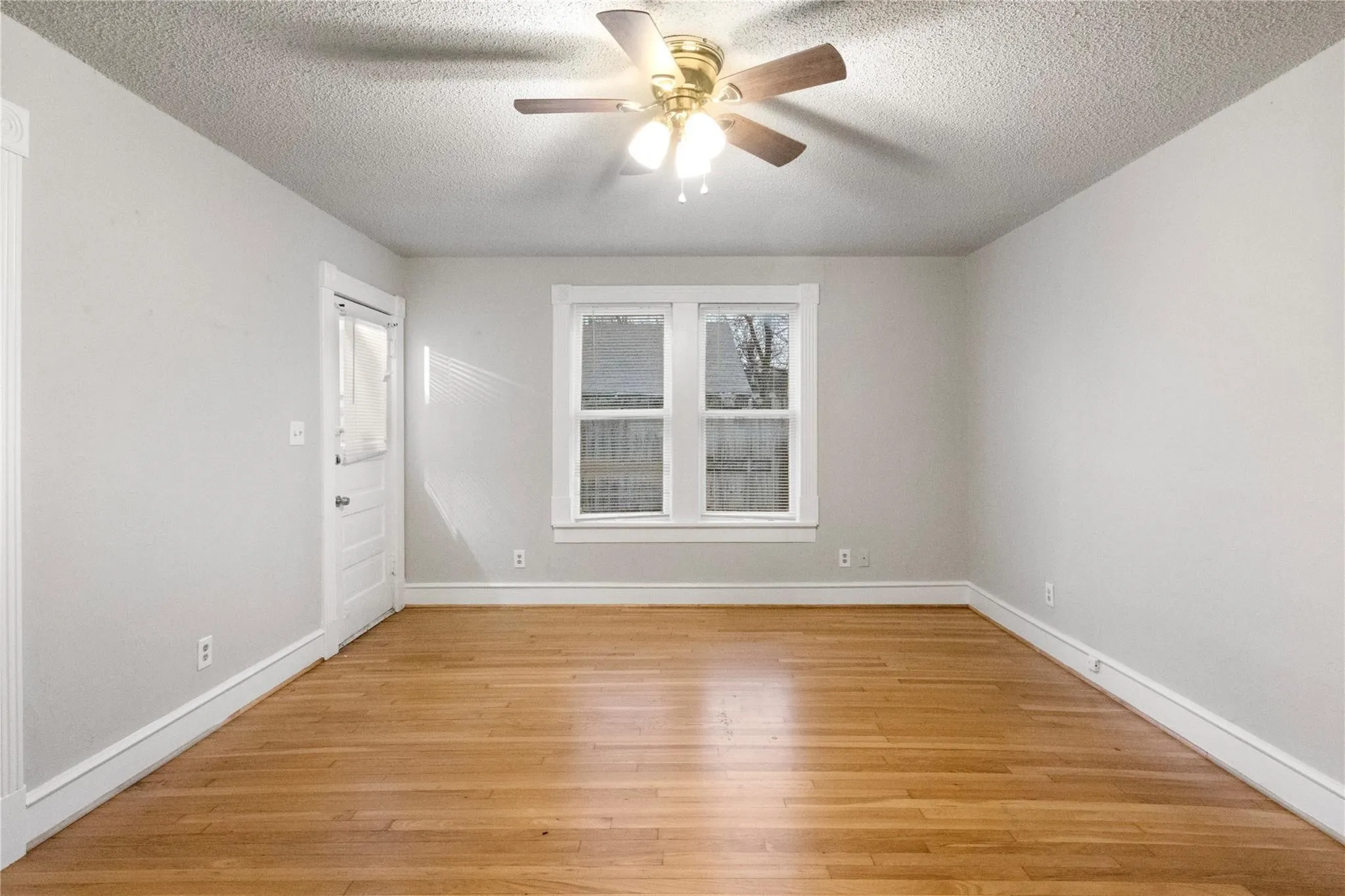 Interior room featuring wood-finish flooring, a multi-pane window with white trim, and a ceiling-mounted light fixture with a central fan