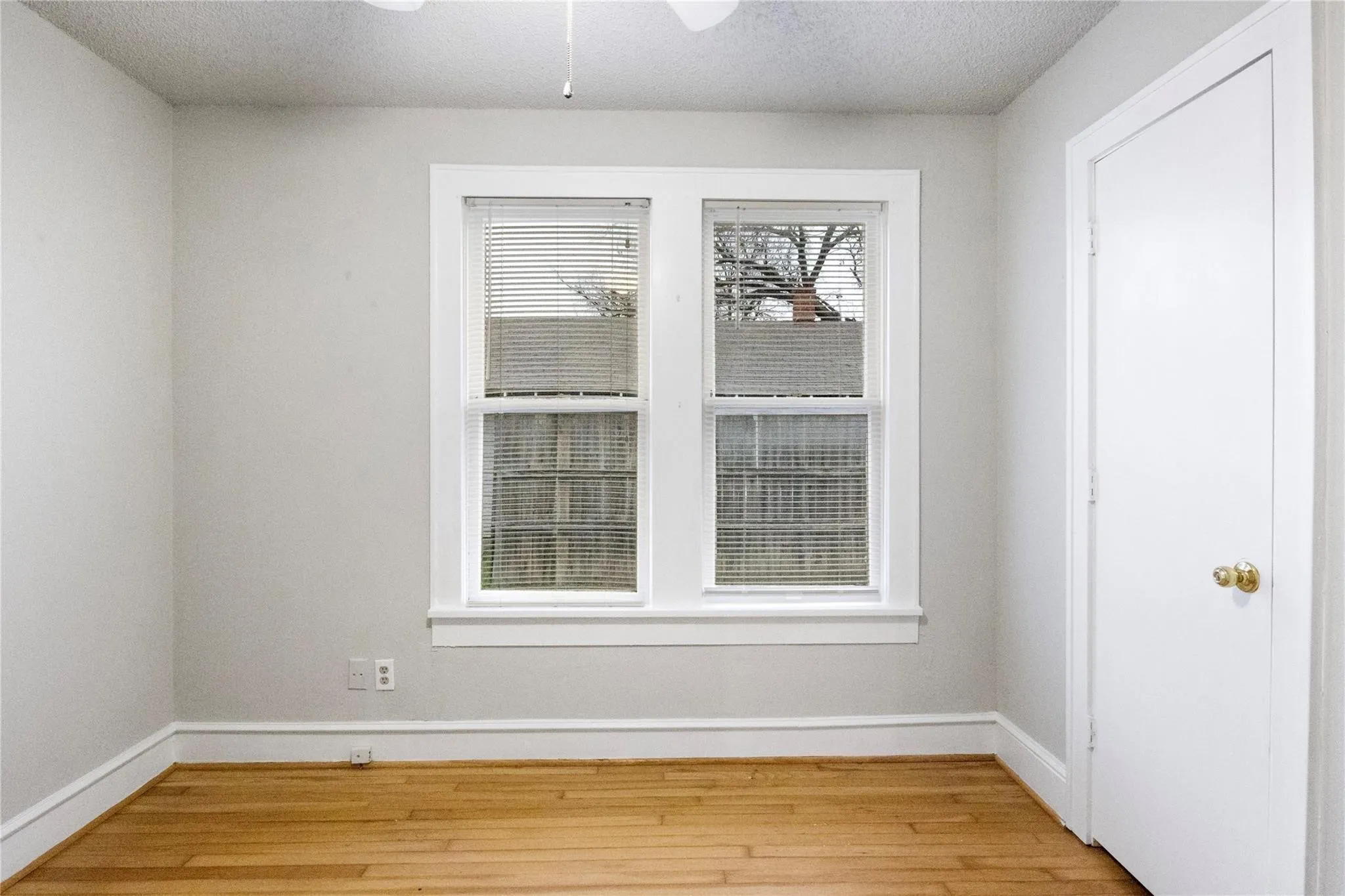 Interior room featuring wood-finish flooring, neutral wall paint, and a double-pane window with white trim