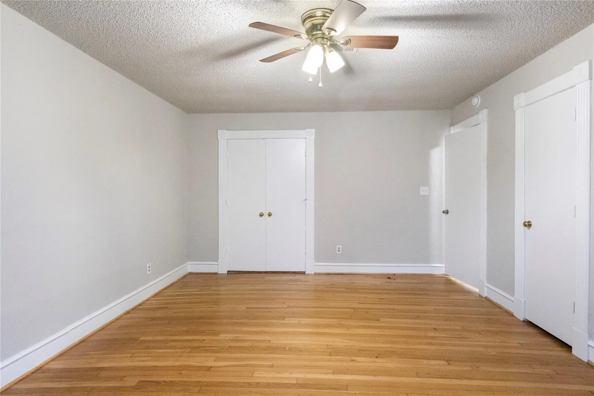 Room featuring wood-finish flooring, white paneled doors, and a ceiling-mounted fan with integrated lighting