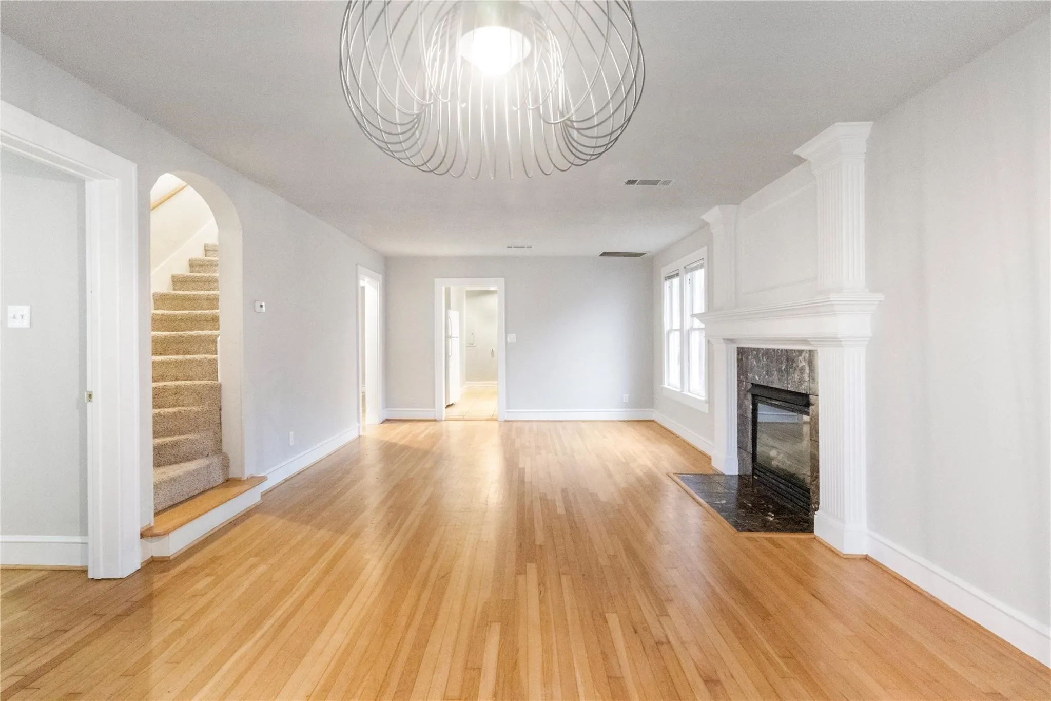 Living area featuring wood-finish flooring, a fireplace with a decorative mantel and hearth, an arched entryway, and a contemporary architectural light fixture