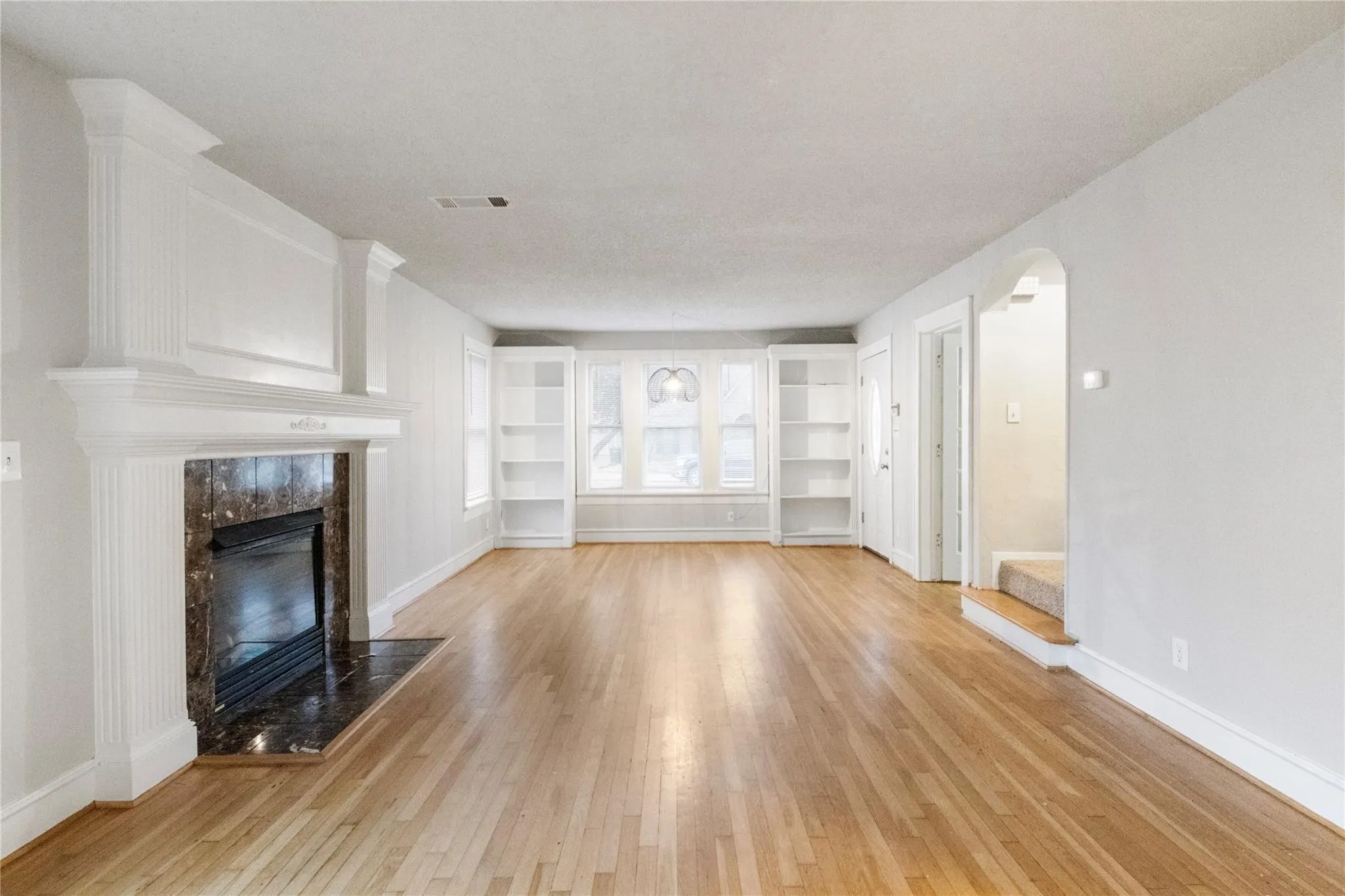 Living area featuring wood-finish flooring, a fireplace with a decorative mantel and stone surround, built-in shelving, and arched entryways