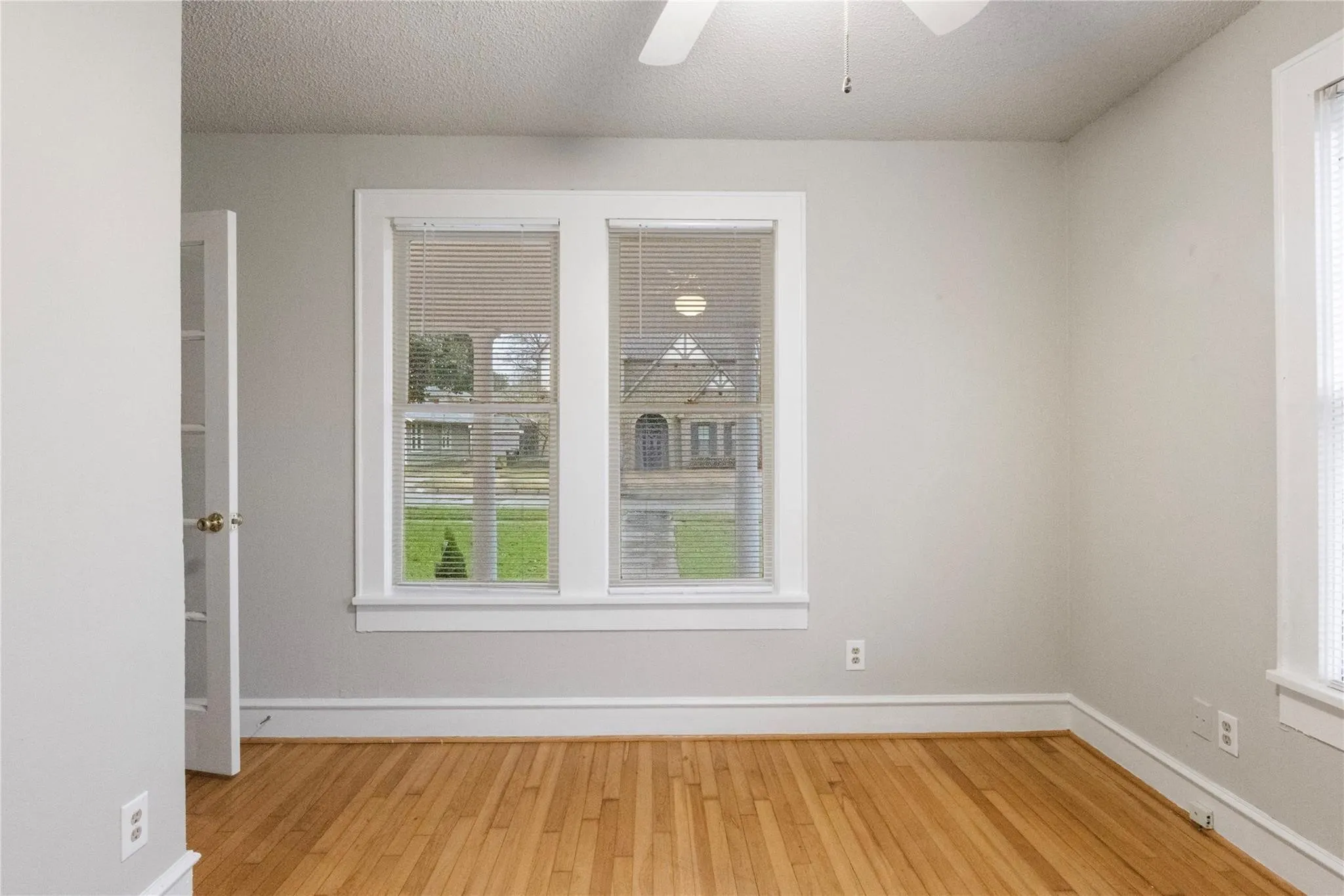 Neutral interior space featuring wood-finish flooring, dual windows with white trim, and a white multi-pane glass-panel door