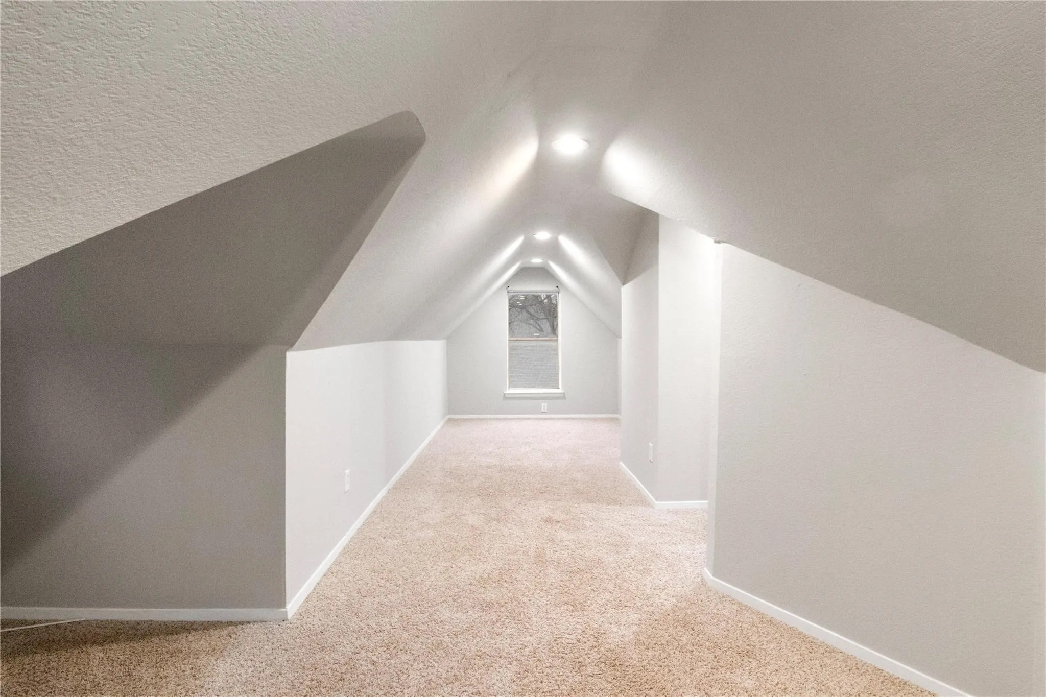 Vaulted ceiling with recessed lighting and neutral-toned wall-to-wall carpeting