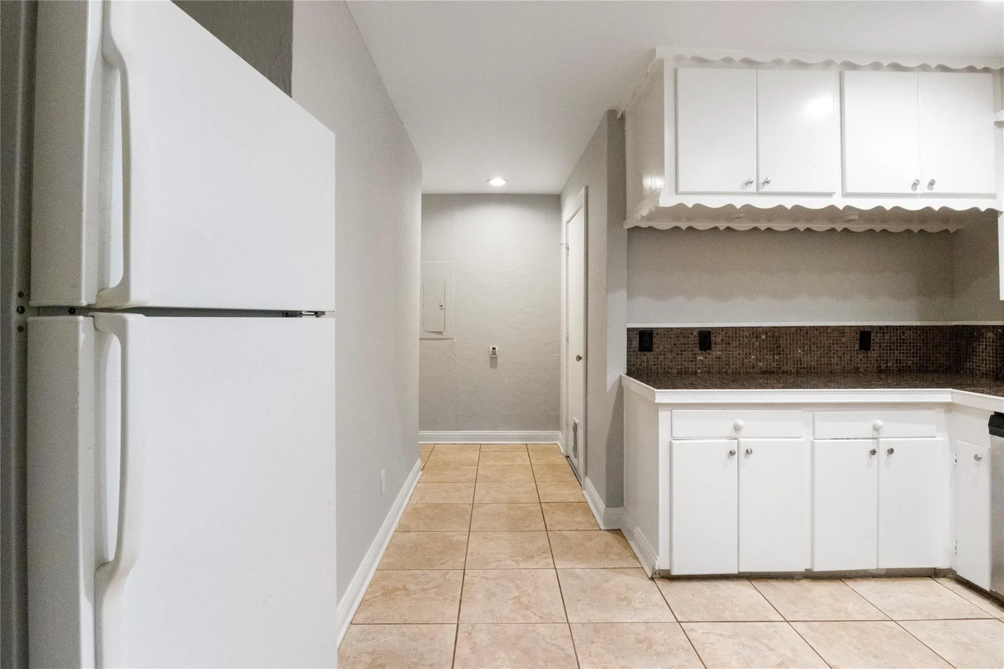 Kitchen featuring white cabinetry with scalloped trim, dark solid-surface countertops, a tiled backsplash, and ceramic floor tiling