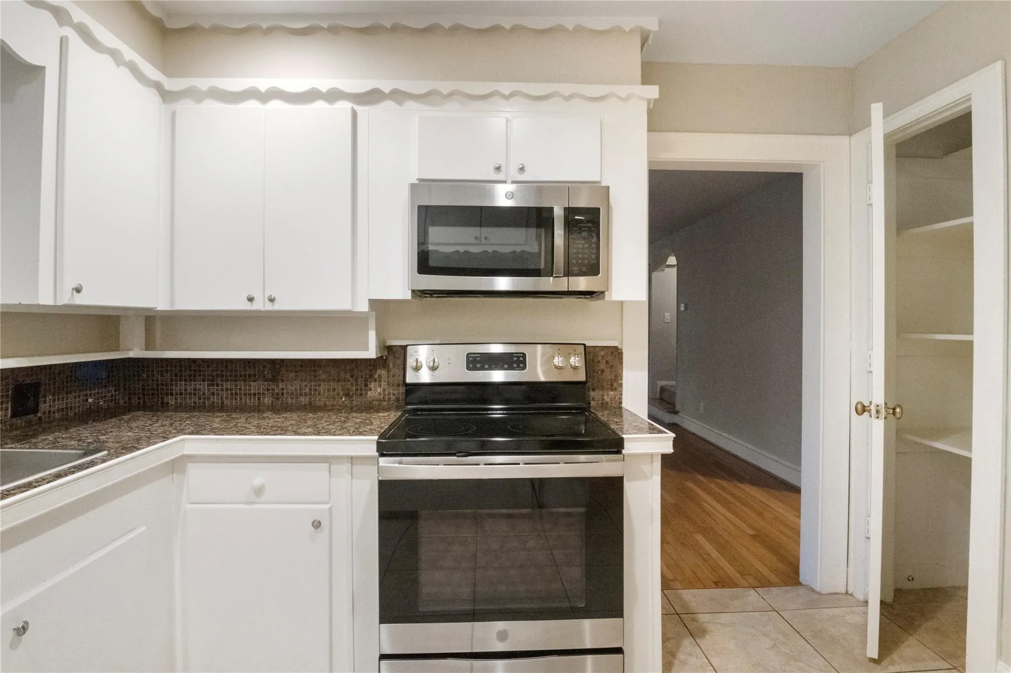 White cabinetry with scalloped trim, stone-finish countertops, stainless steel appliances, and built-in pantry shelving