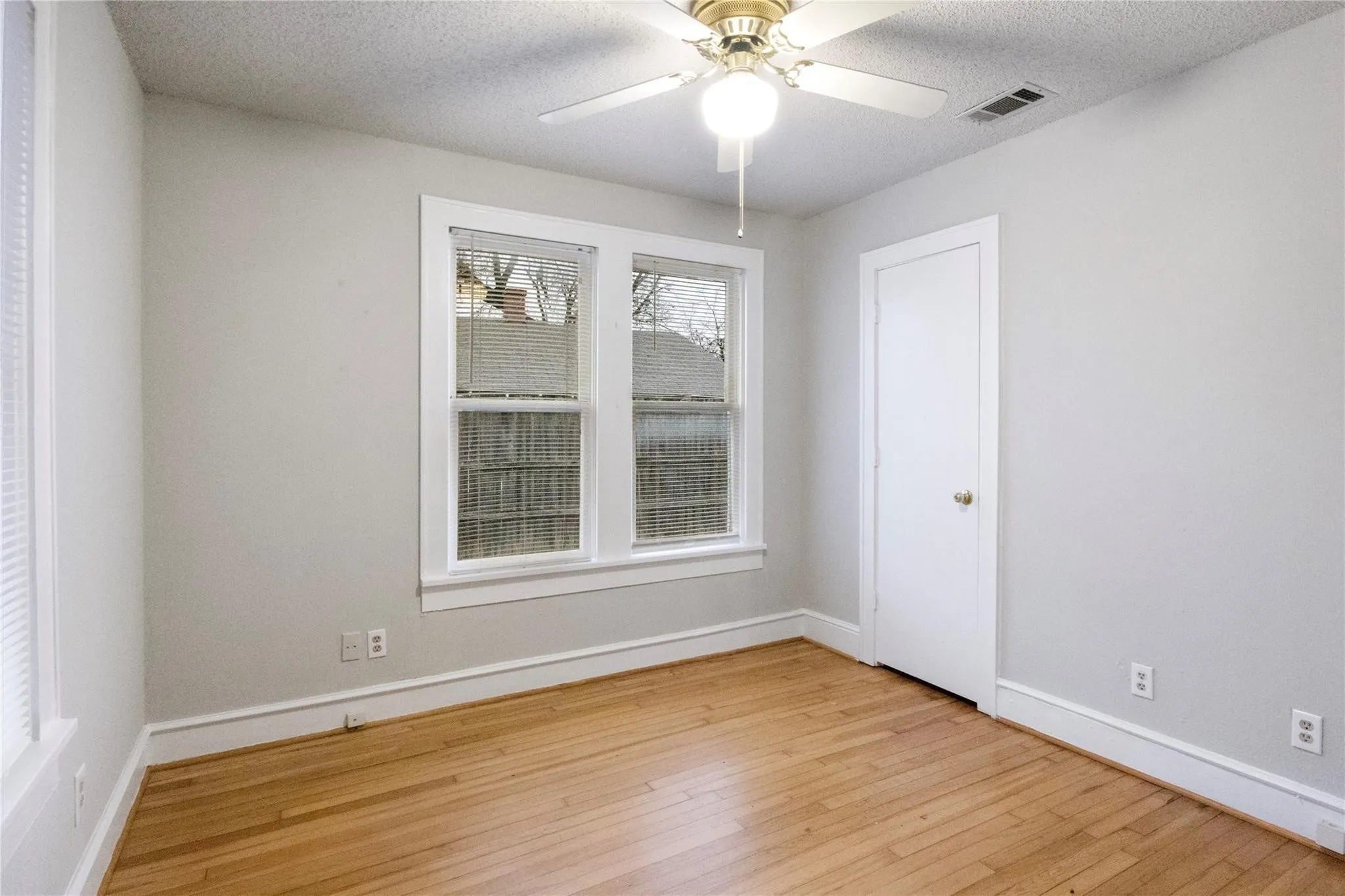 Interior space featuring wood-finish flooring, neutral wall paint, white trim, dual-pane windows, and a ceiling-mounted light fixture with fan