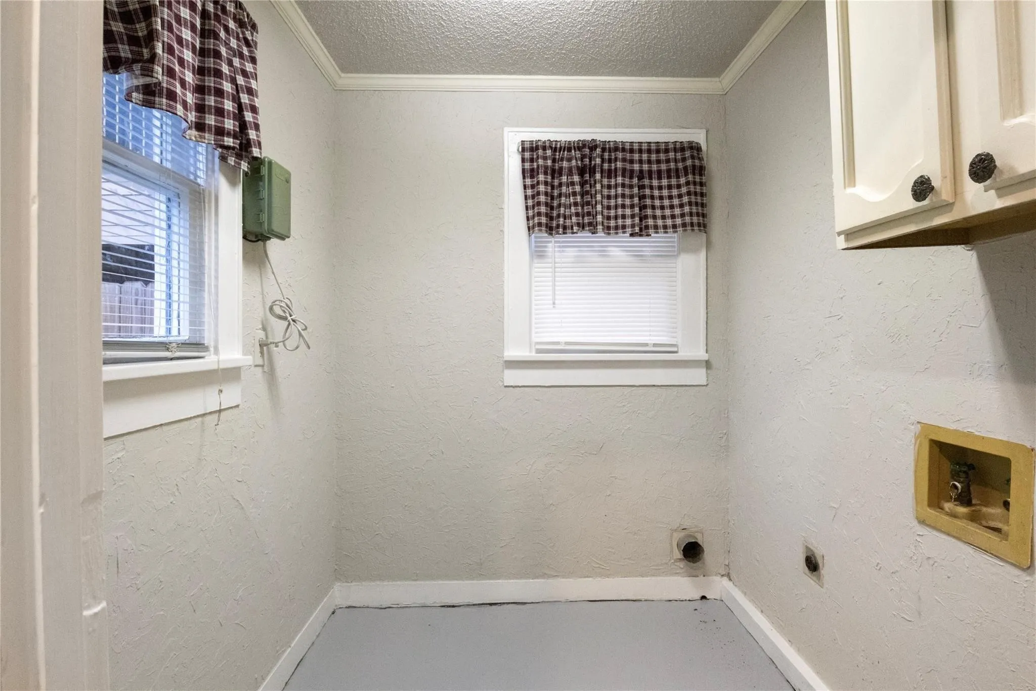 Textured wall finishes, built-in upper cabinetry, dual windows with white casing, and dedicated laundry utility hookups