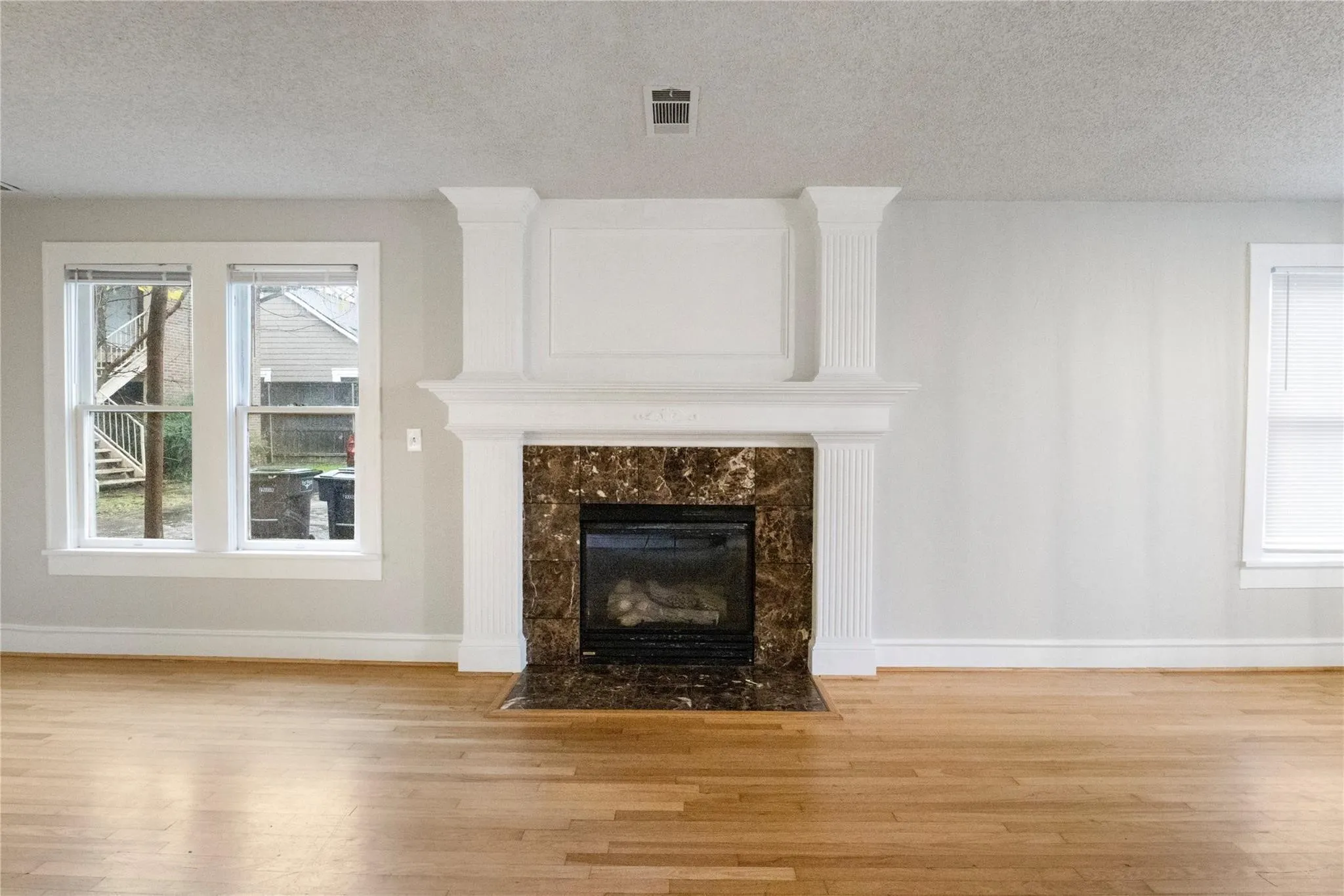 Fireplace featuring a stone-patterned surround, decorative white columns, a custom mantel, wood-finish flooring, and multi-pane windows