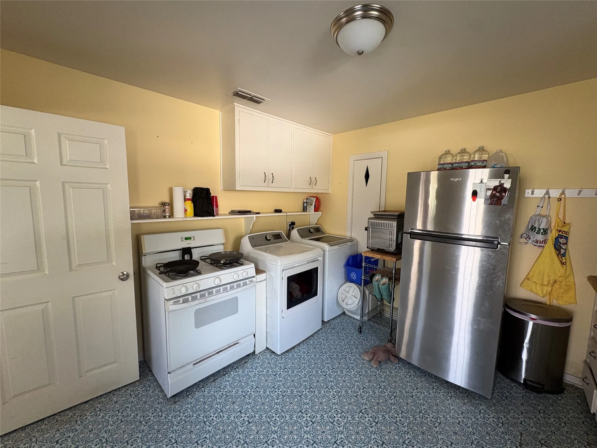 Utility area featuring patterned tile flooring, white wall-mounted cabinetry, white gas range, and stainless steel refrigerator
