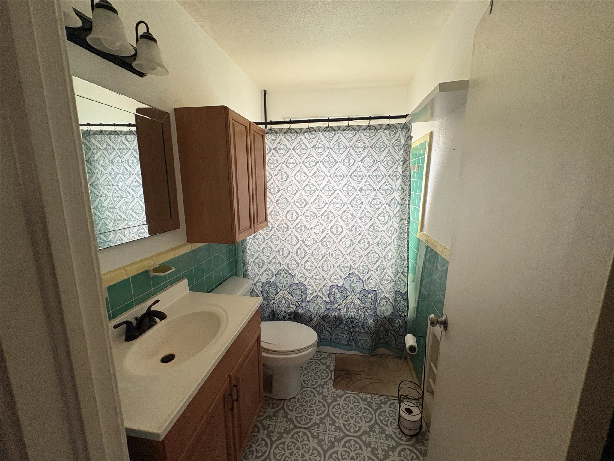 Bathroom featuring a vanity with integrated sink, wood-finish cabinetry, wall-mounted mirror, decorative ceramic tile backsplash, and patterned flooring