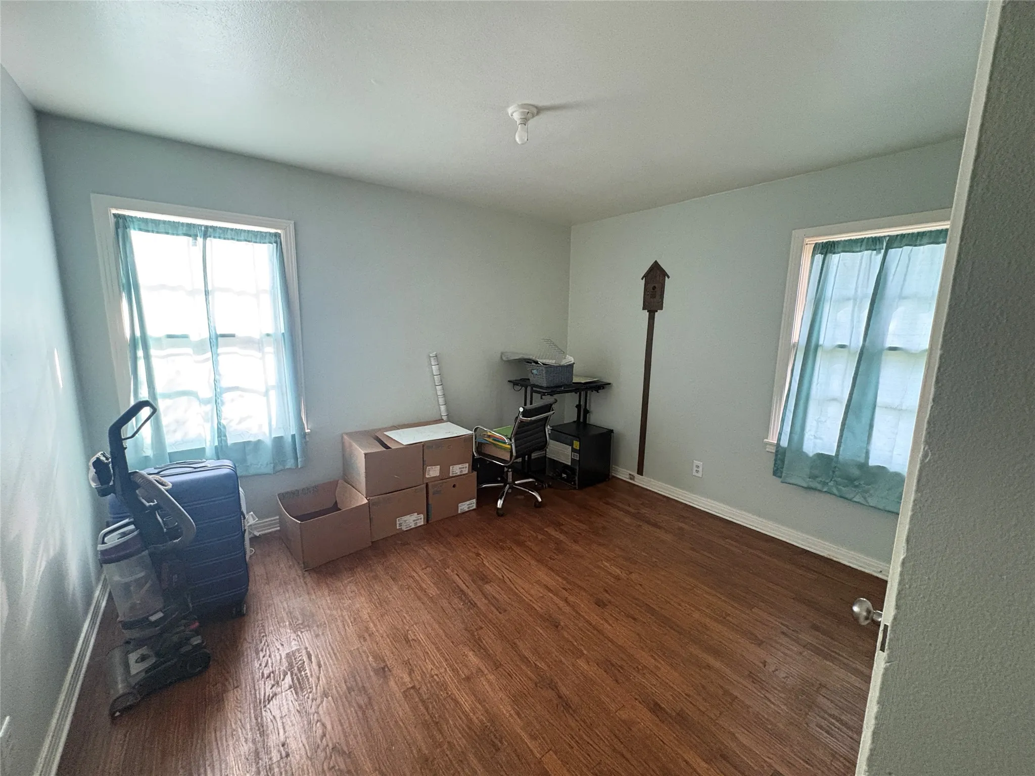 Wood-finish flooring, two windows with white trim, and neutral wall paint