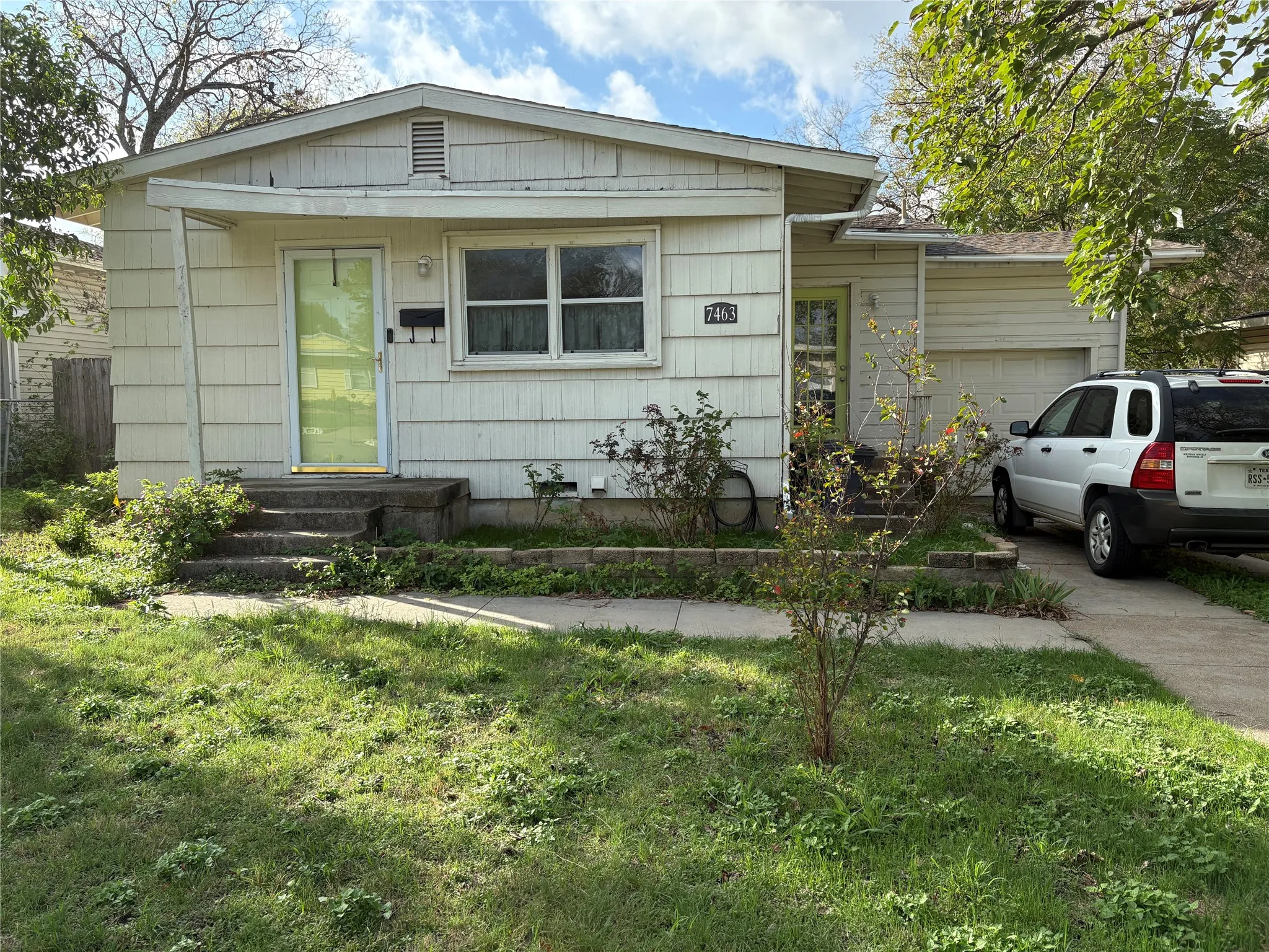 Single-story exterior featuring light-colored horizontal siding, a gabled roofline, an attached garage, and a concrete driveway