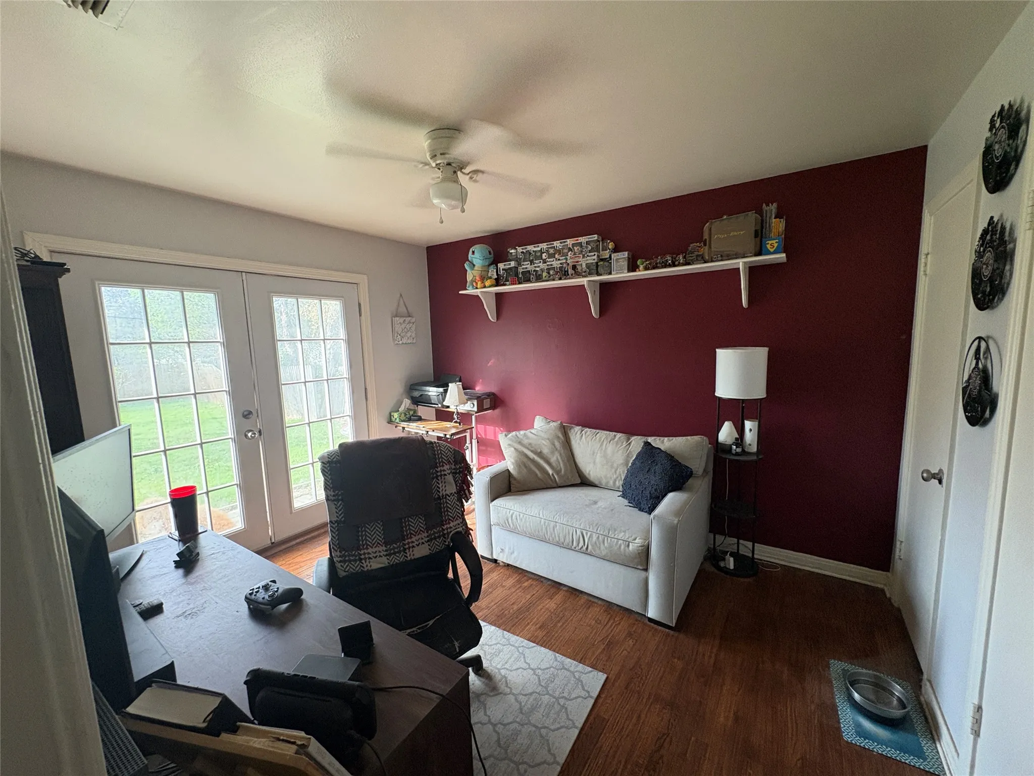 Wood-finish flooring, ceiling fan with integrated light, accent wall, and glass-paned double doors