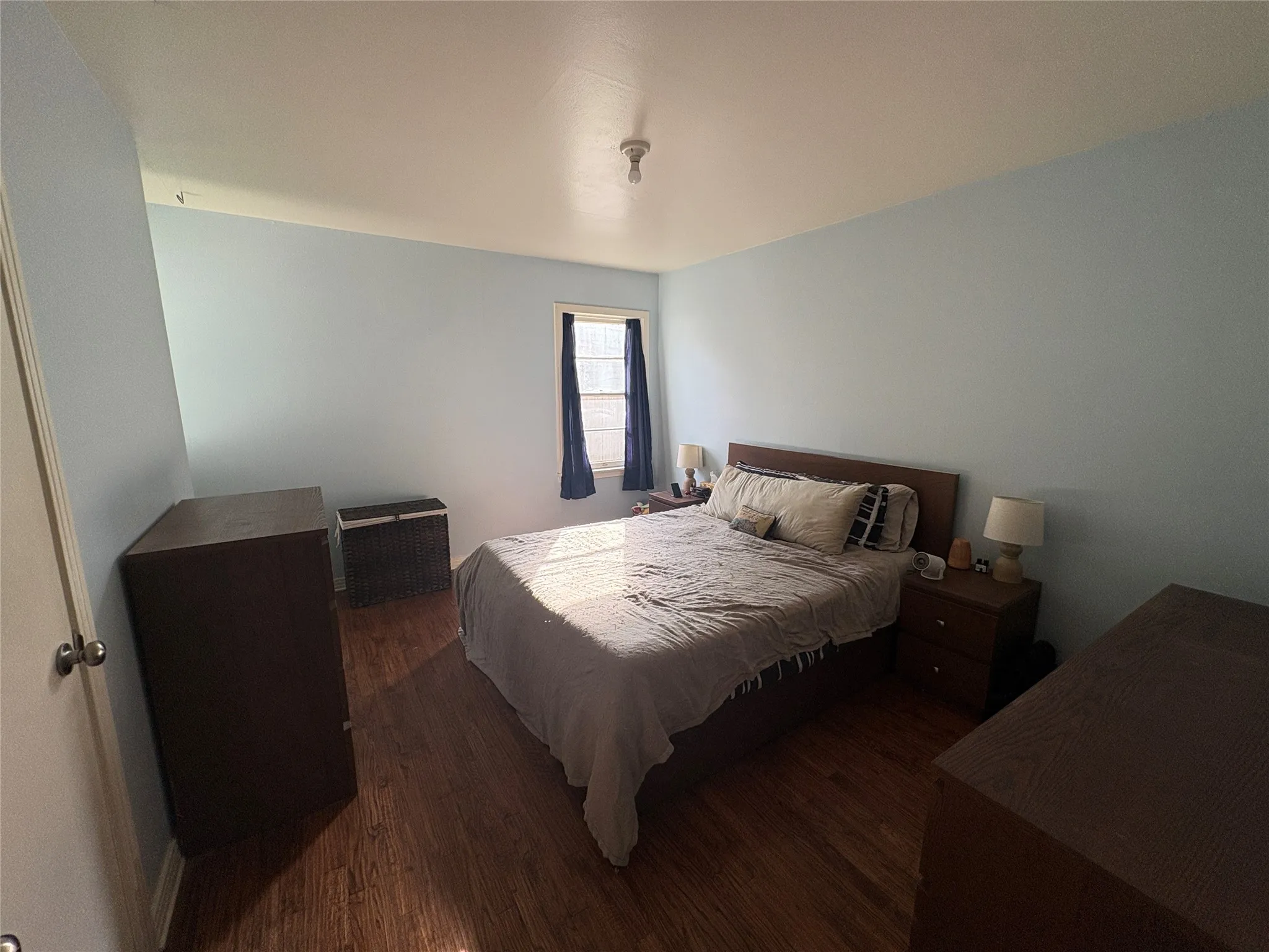 Room featuring wood-finish flooring, light blue walls, and a single-pane window