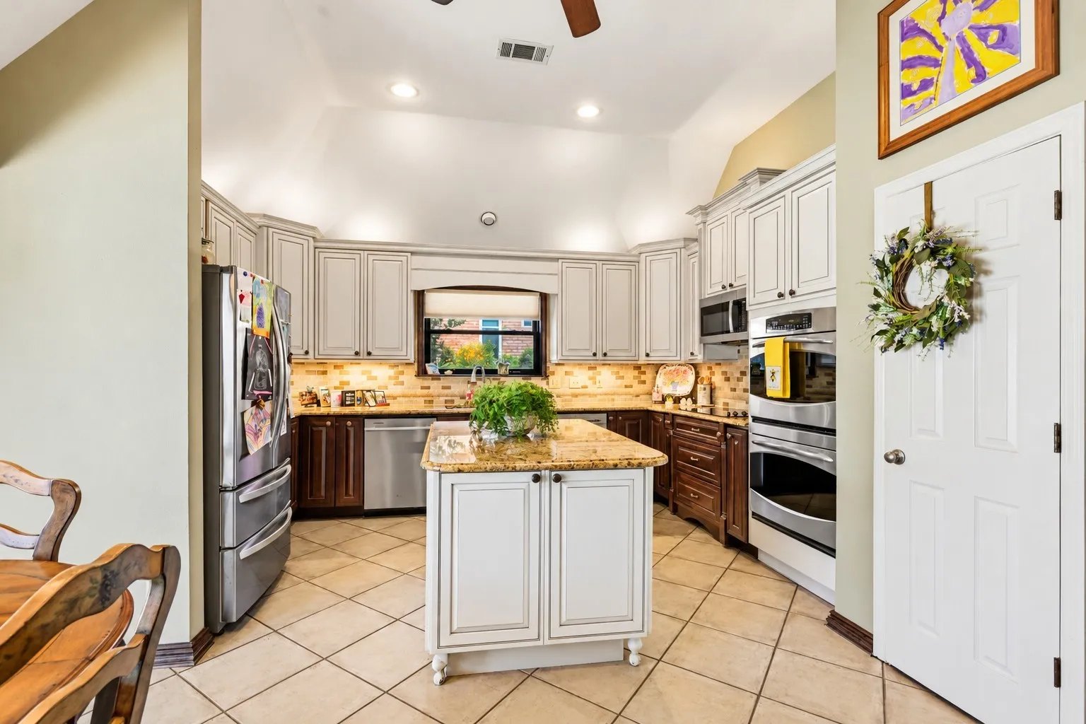 Spacious kitchen featuring abundant cabinetry with elegant crown molding, contrasting light upper cabinets and rich wood lower cabinets, and a warm tile backsplash.