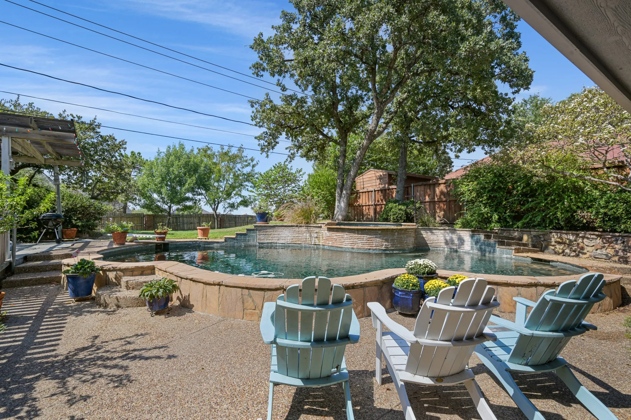 Enjoy your own backyard retreat featuring a sparkling swimming pool with a raised stone accent wall and beautifully landscaped surroundings. The expansive patio offers plenty of space for outdoor seating and entertaining, while mature trees provide natural shade and a peaceful setting.