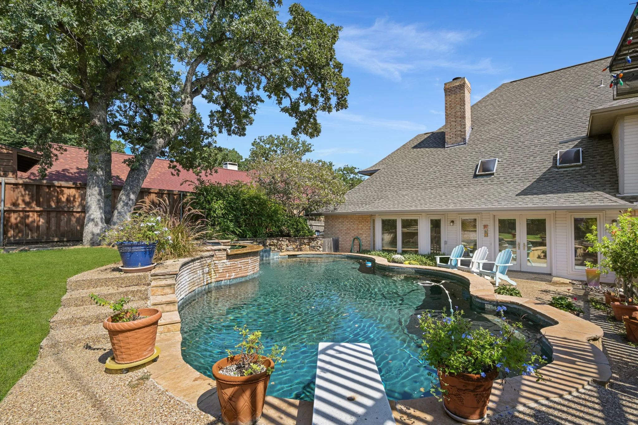 Inviting pool has a diving board and is shaded by a gorgeous mature tree.