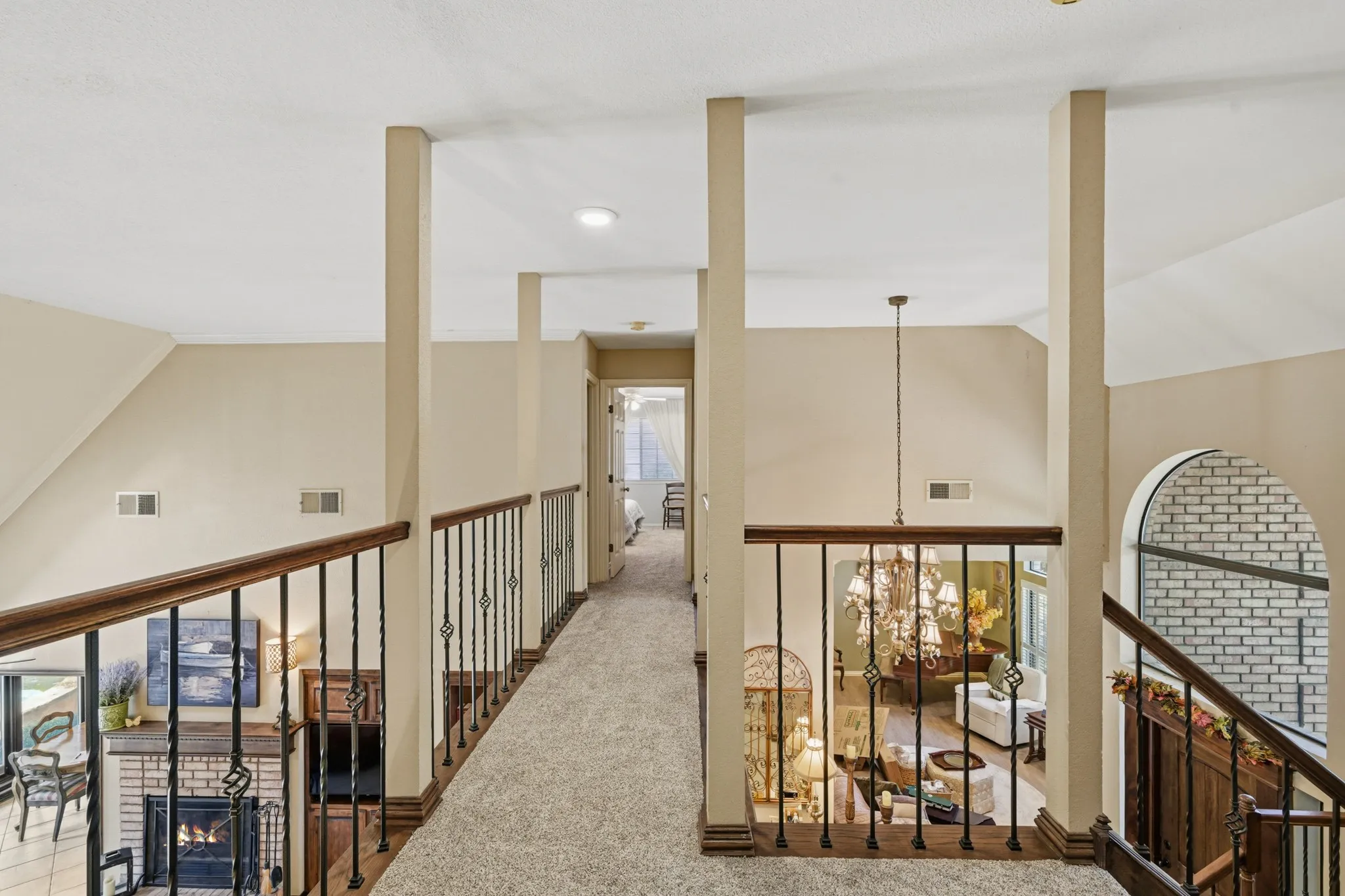 Upstairs landing features an open overlook to the main living area below, highlighted by decorative wrought-iron railings with rich wood handrails and trim.  An open walkway create an airy, spacious feel while offering views of the home's inviting living spaces and architectural details.