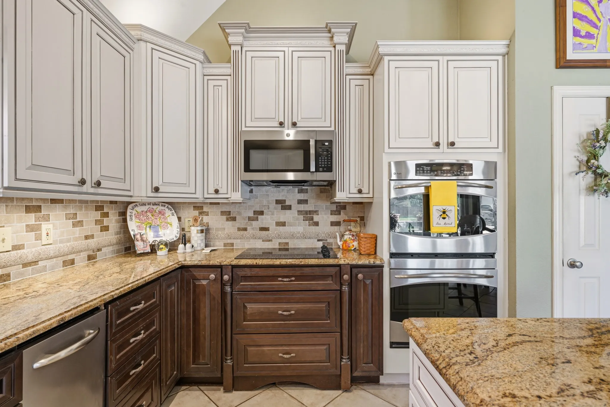 Stainless steel appliances include a French-door refrigerator, built-in microwave, and double ovens. A center island with granite countertops provides additional workspace, while ceramic tile flooring, recessed lighting, and a vaulted ceiling complete this inviting and functional kitchen.