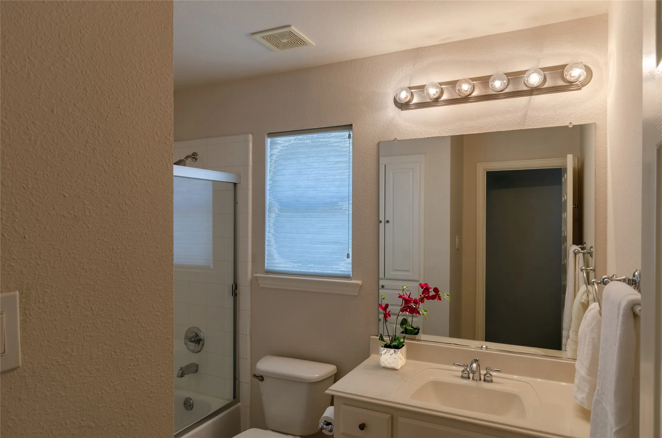 Bathroom featuring a vanity with a solid-surface countertop, rectangular undermount sink, multi-bulb wall-mounted light fixture, large wall-mounted mirror, and a tub-shower combination with sliding glass doors