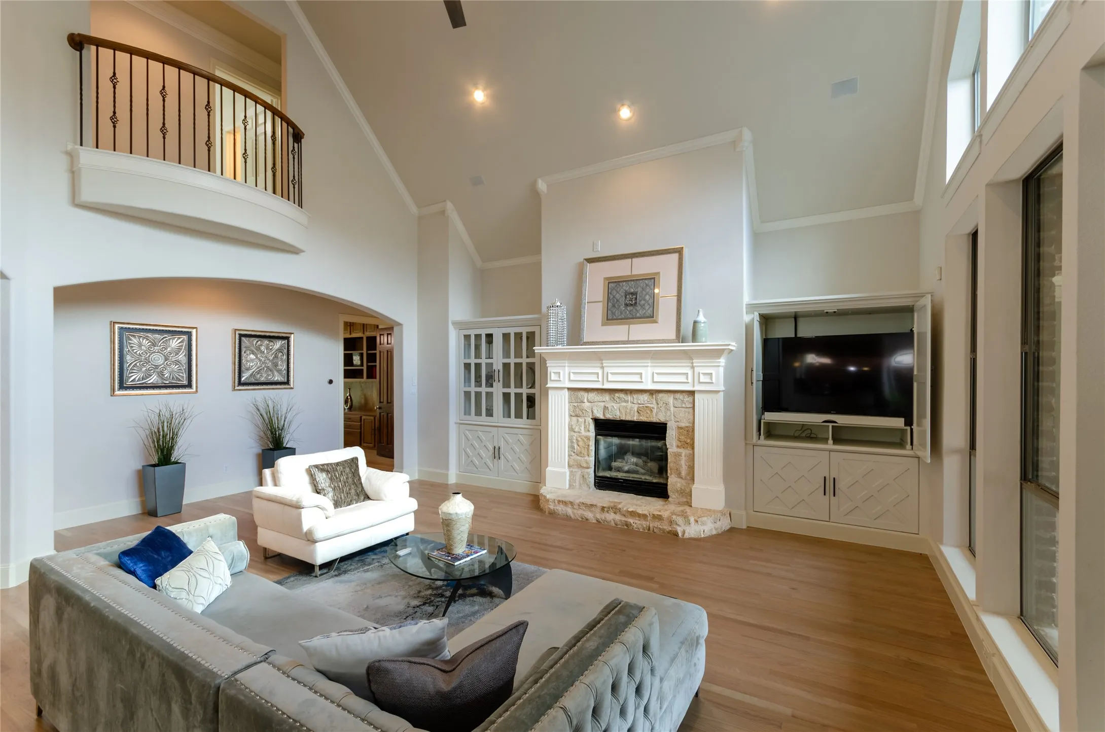 Vaulted ceilings with an overlook balcony, stone-faced fireplace with a detailed mantel, wood-finish flooring, and built-in custom cabinetry