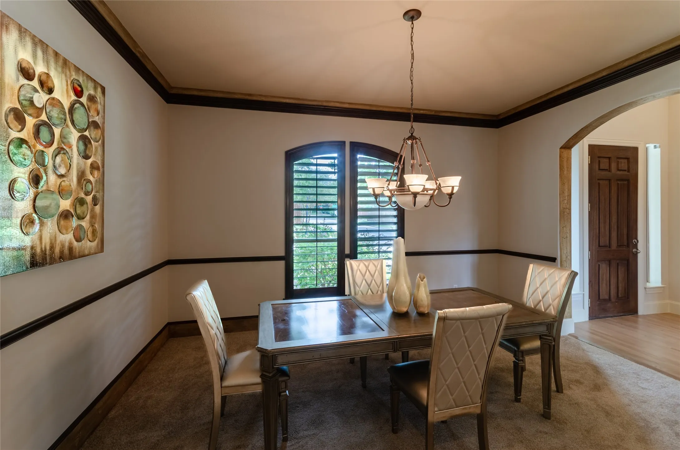 Dining area featuring dark wood crown molding, chair rail trim, arched window with plantation shutters, and a multi-arm chandelier