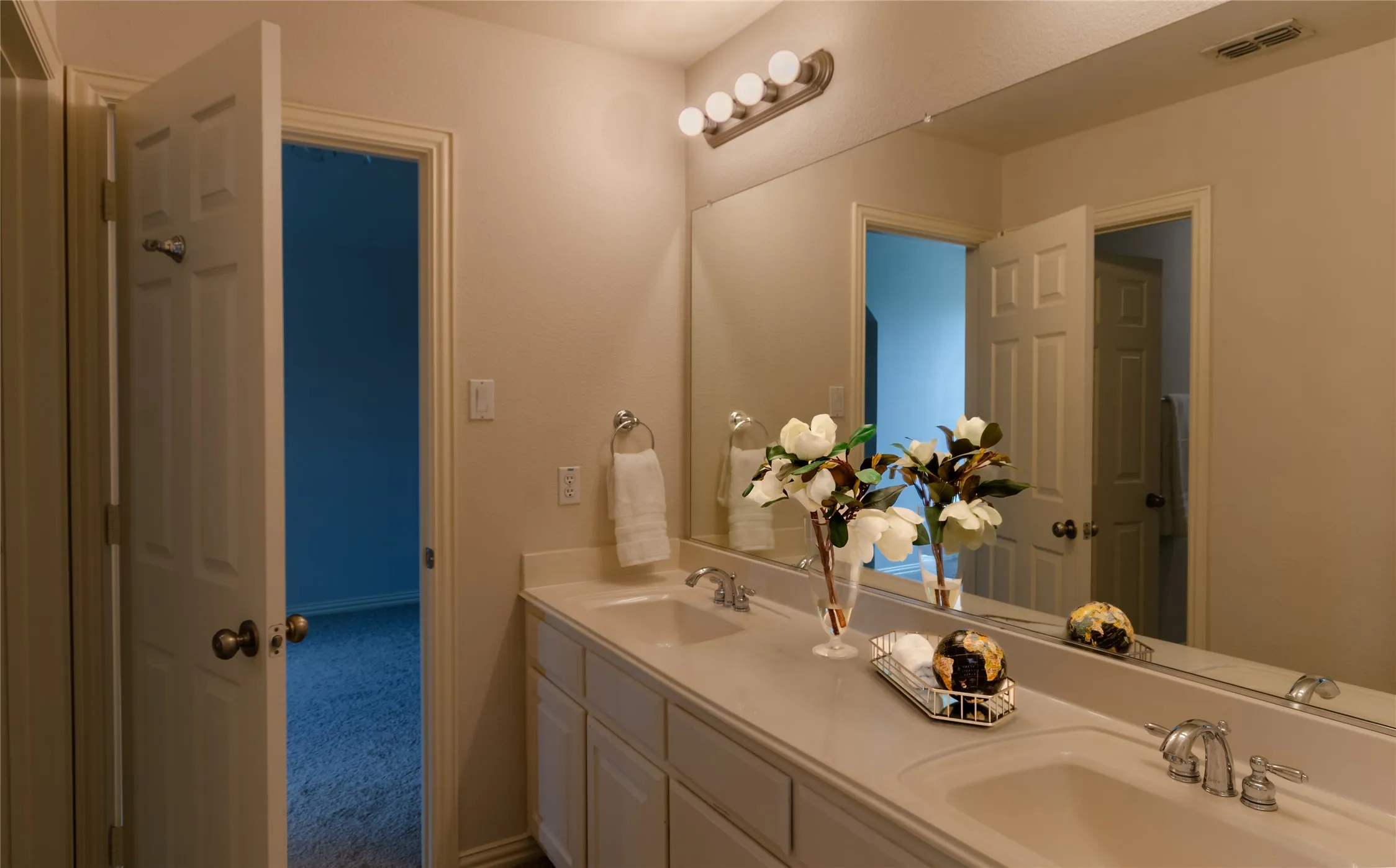 Dual-sink vanity with a solid-surface countertop, full-width wall mirror, and chrome-finish hardware