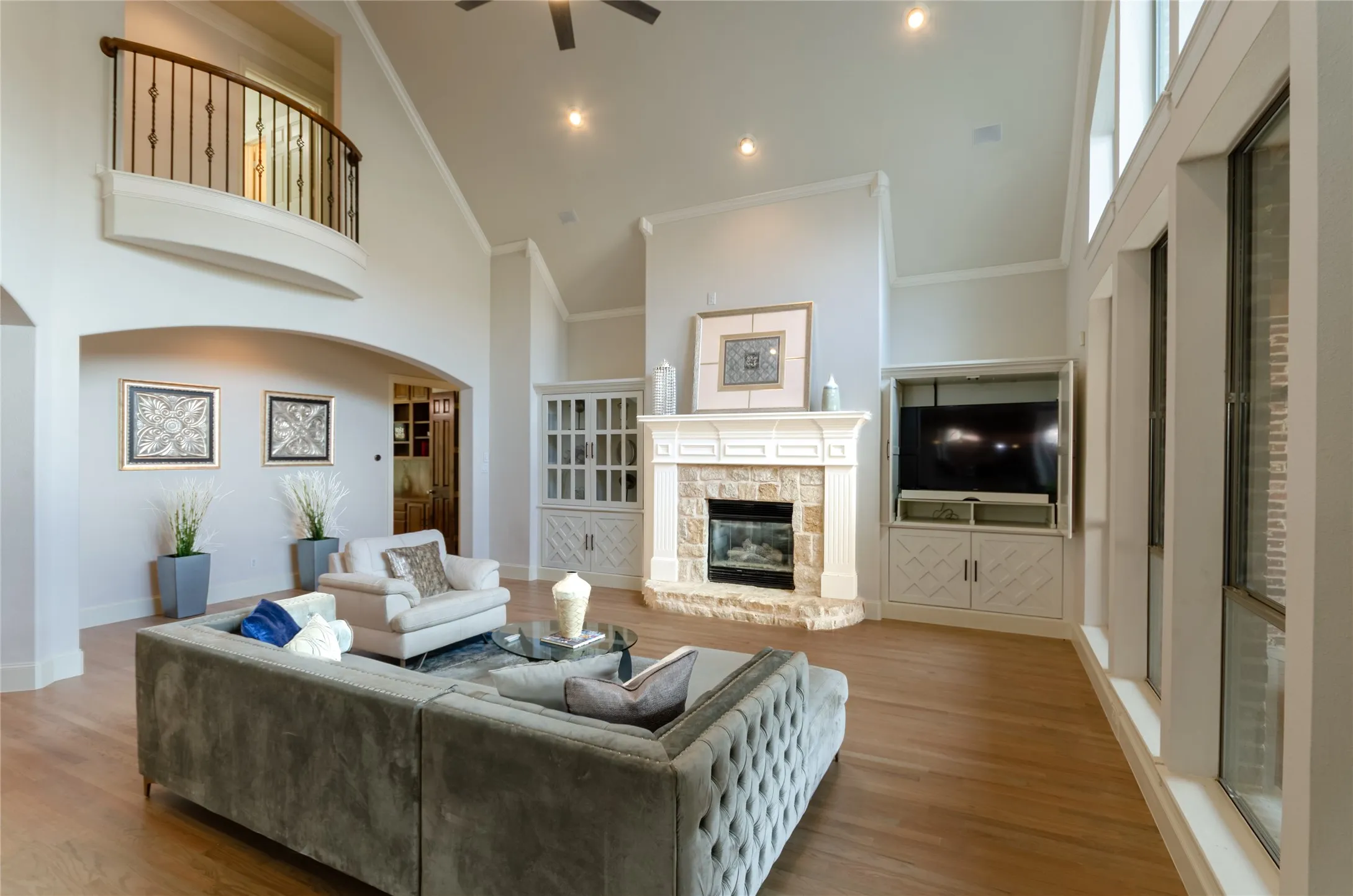 Vaulted ceilings, stone-surround fireplace with a custom mantle, built-in cabinetry, wood-finish flooring, and an elevated overlook with iron railing