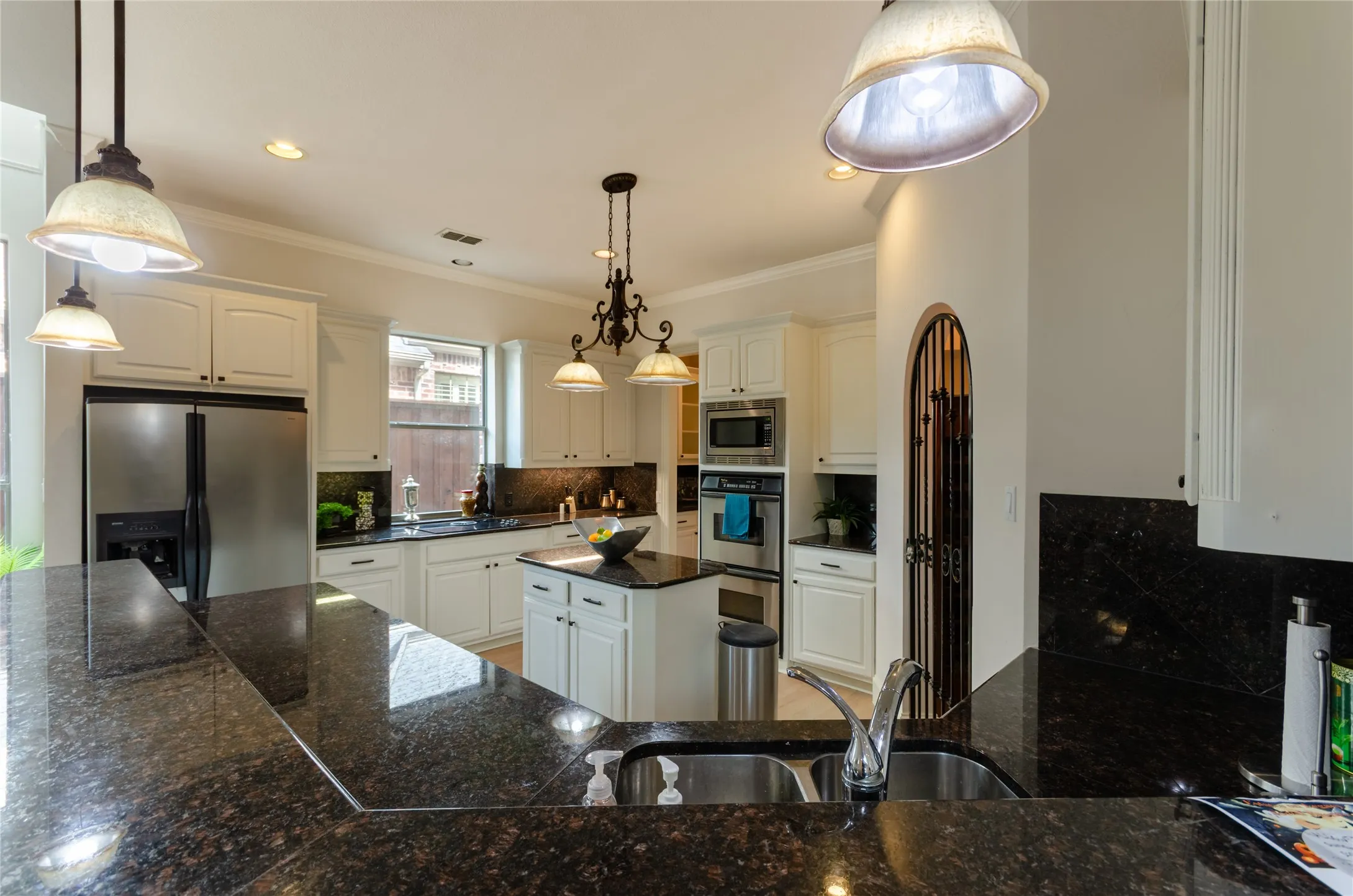 Kitchen featuring stone countertops, stainless steel built-in double ovens, a center island, white cabinetry, and decorative pendant lighting