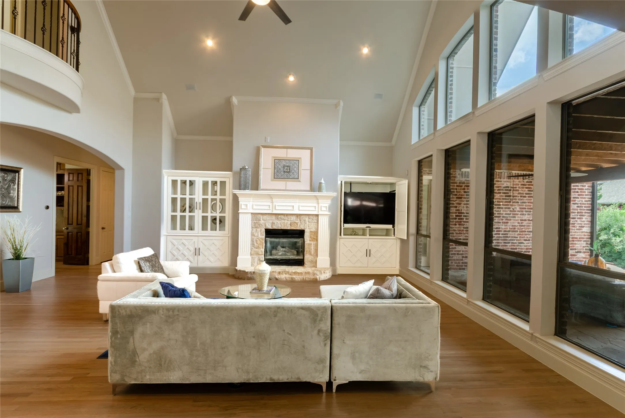 Vaulted ceilings with recessed lighting, stone-surround fireplace, built-in cabinetry, wood-finish flooring, and expansive windows