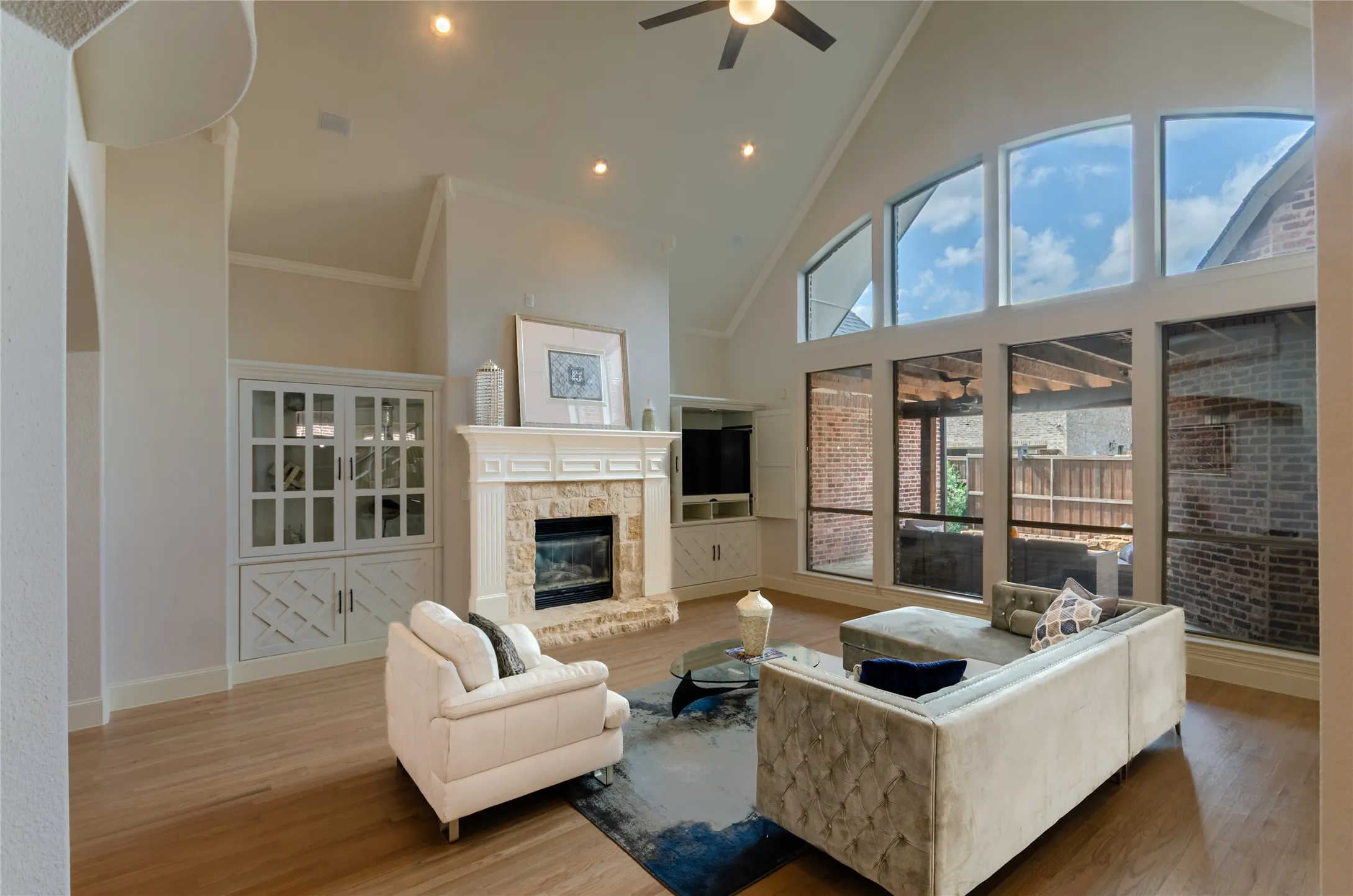 Vaulted ceilings featuring a ceiling fan, stone-surround fireplace with a detailed mantel, built-in cabinetry, and floor-to-ceiling windows with wood-finish flooring