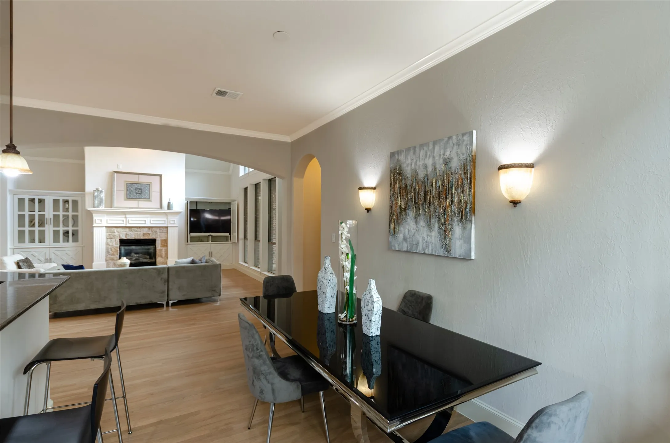 Open-concept interior featuring light wood-finish flooring, crown molding, arched entryways, and two wall-mounted decorative light fixtures
