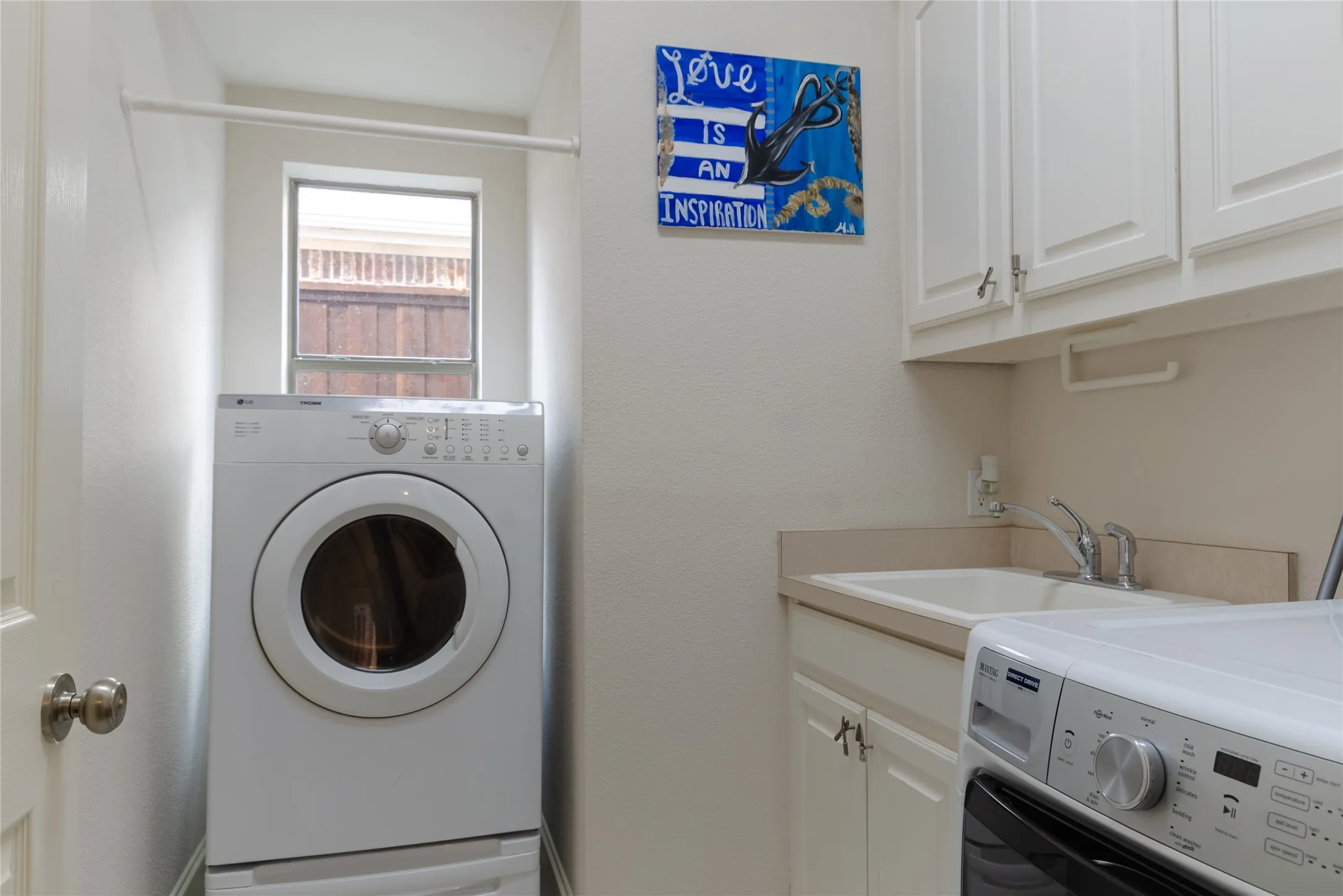 Laundry room featuring white cabinetry, a built-in utility sink with a faucet, and a wall-mounted hanging rod