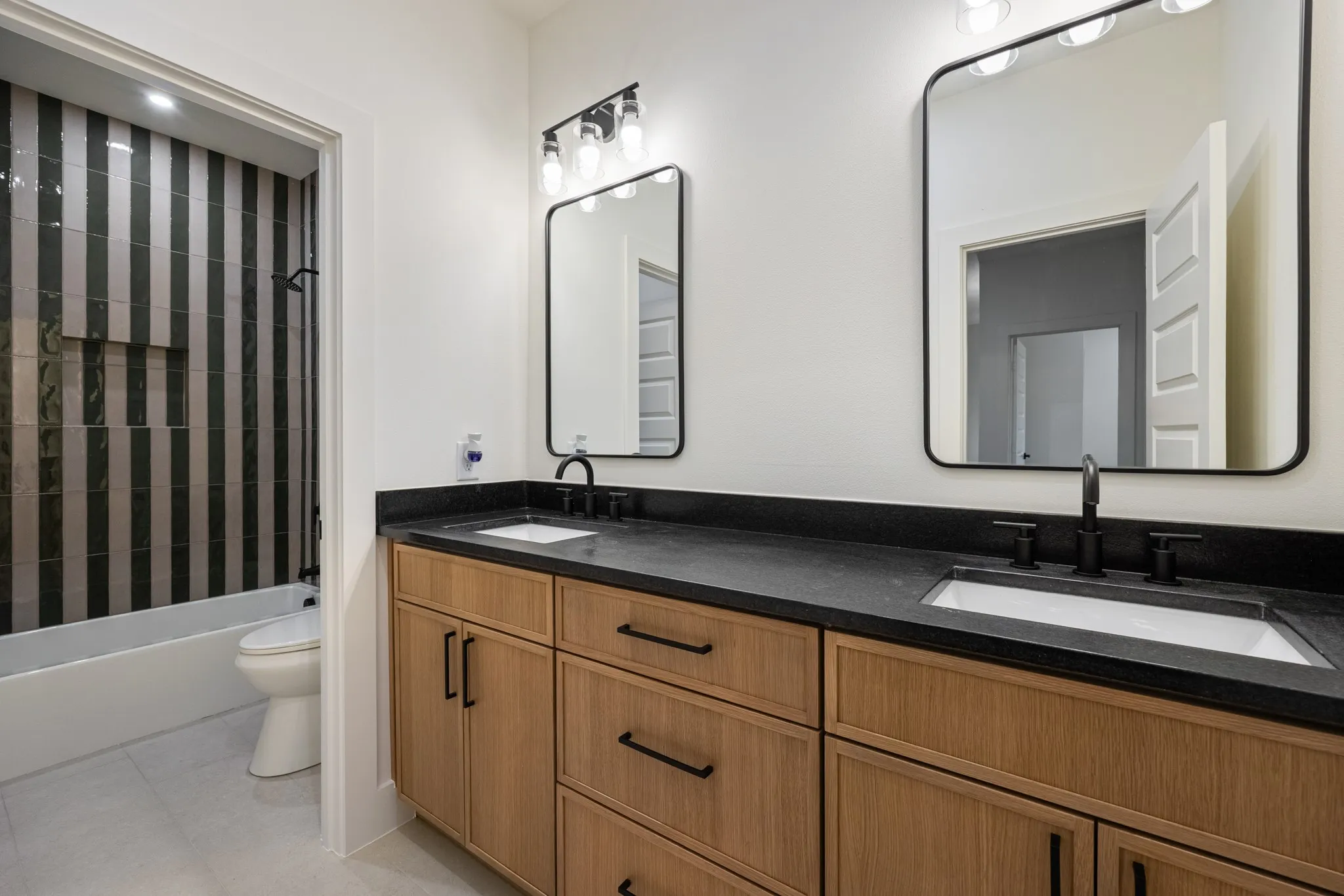 Guest bath with striped shower tile and dual vanity.