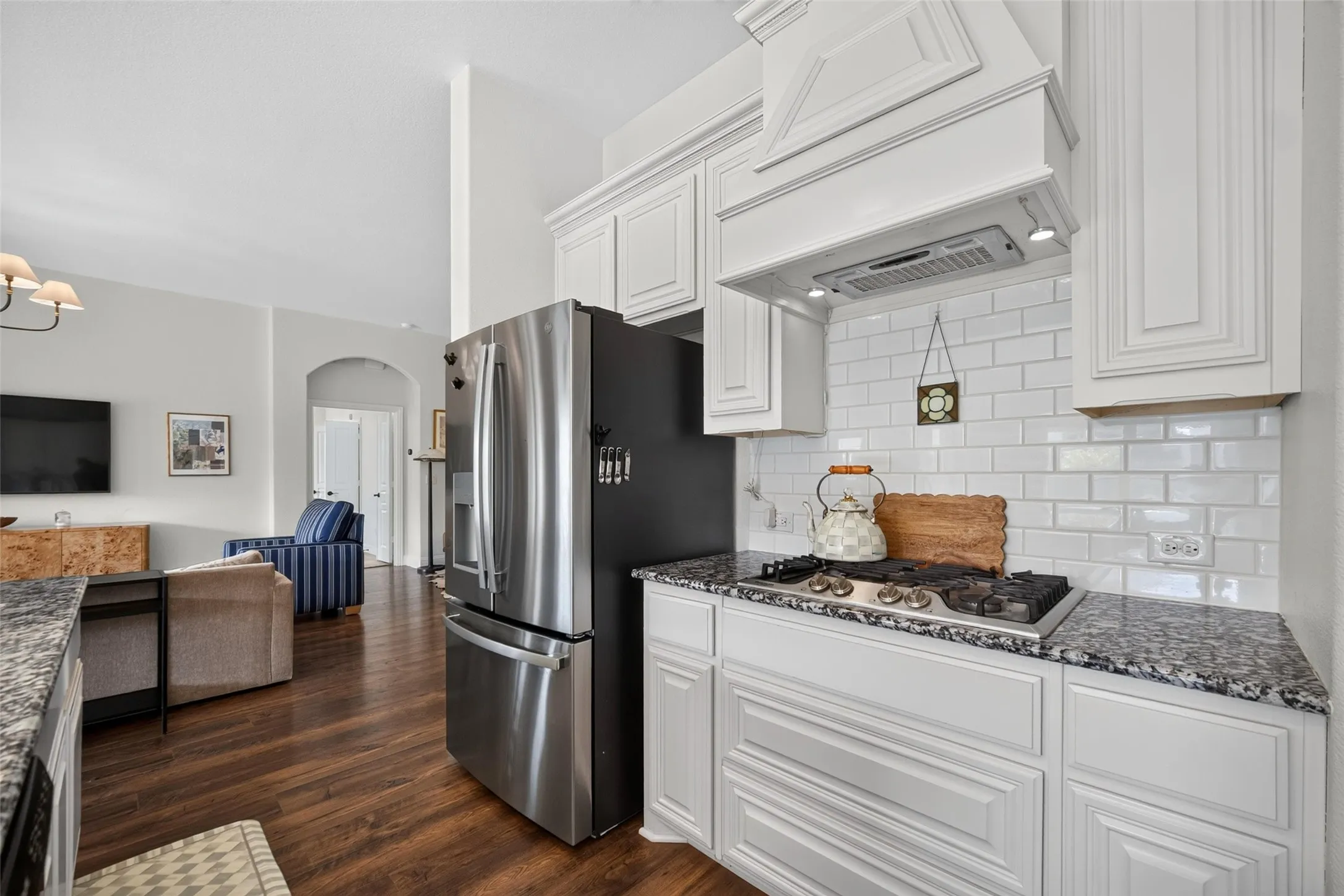 Kitchen featuring white cabinetry, subway tile backsplash, stone-finish countertops, stainless steel appliance suite, and wood-finish flooring