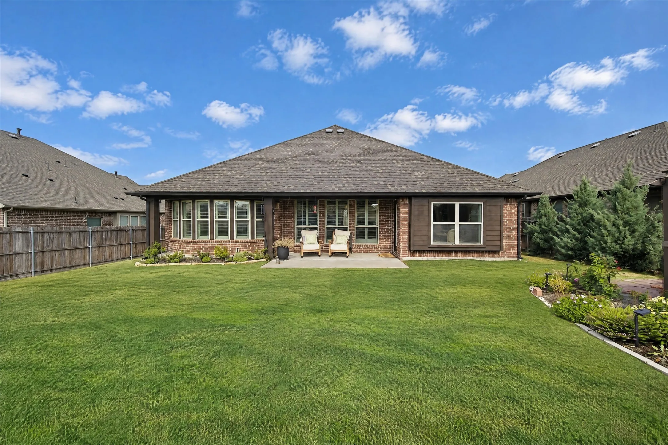 Brick exterior featuring a concrete patio, a deep-set roofline, multiple paneled windows, and a fully fenced backyard
