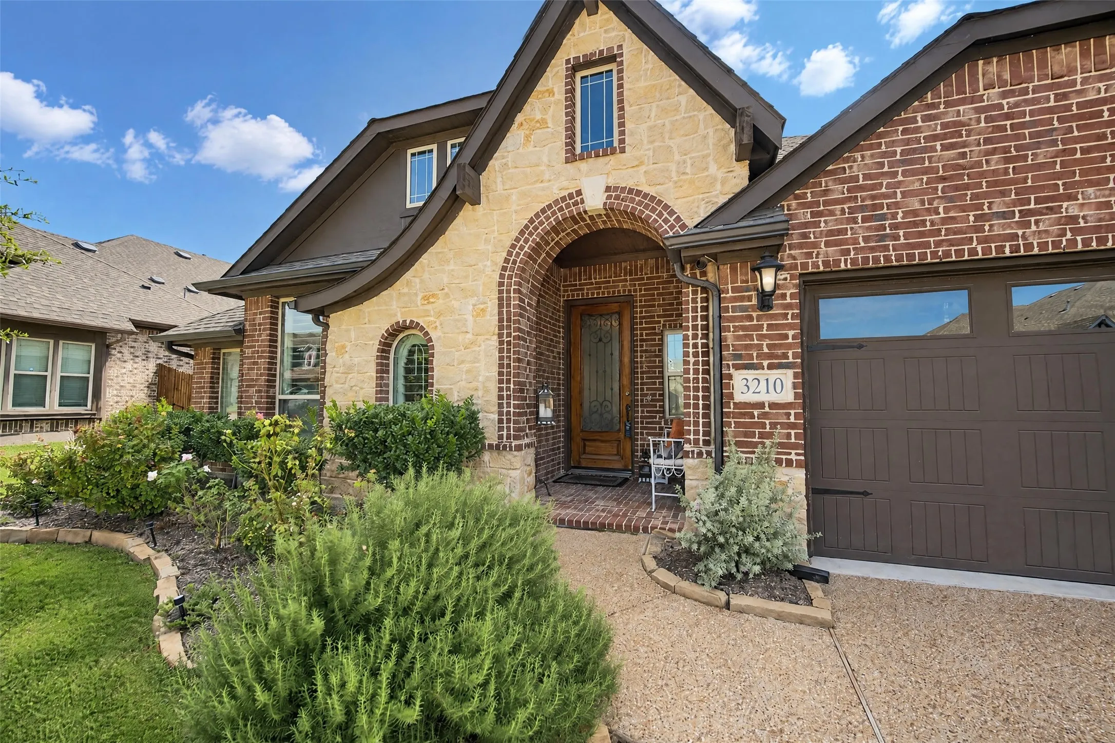 Stone and brick facade featuring an arched entryway, decorative wood front door with glass inlay, and an attached multi-car garage with carriage-style detailing