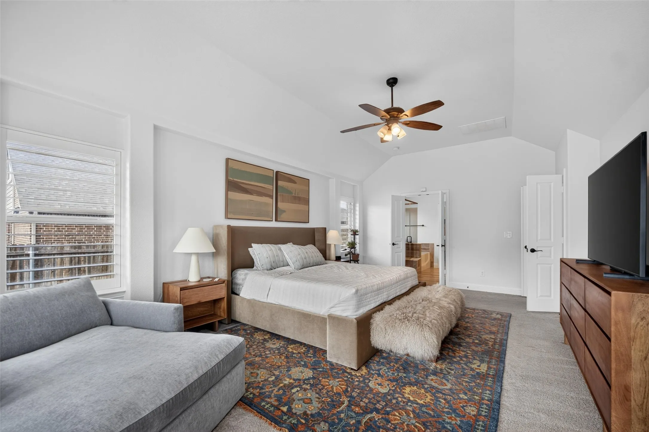 Vaulted ceilings, neutral carpeting, window shutters, and a ceiling fan with integrated lighting