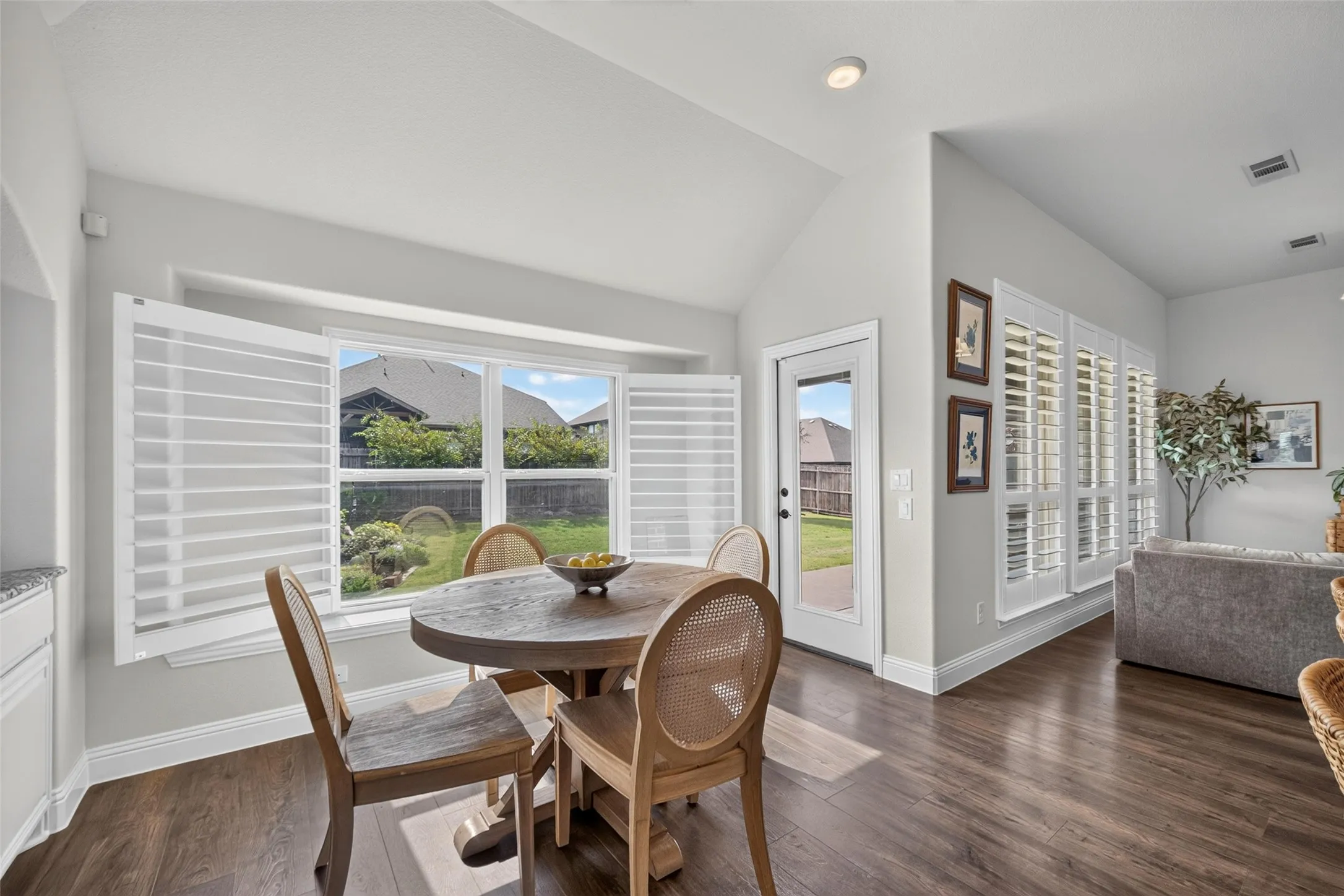 Vaulted ceiling featuring white shutters on expansive windows, wood-finish flooring, and a glass-paneled exterior door