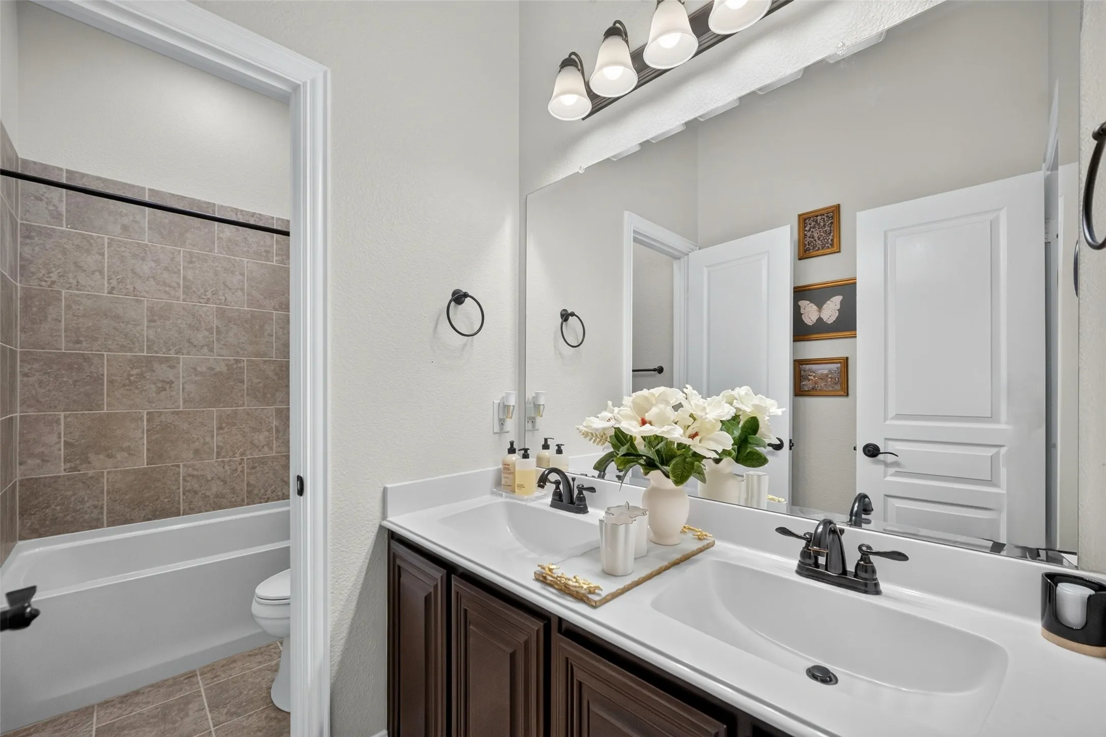 Double vanity featuring a light-toned countertop, rectangular undermount sinks, dark wood-finish cabinetry, and matte black fixtures
