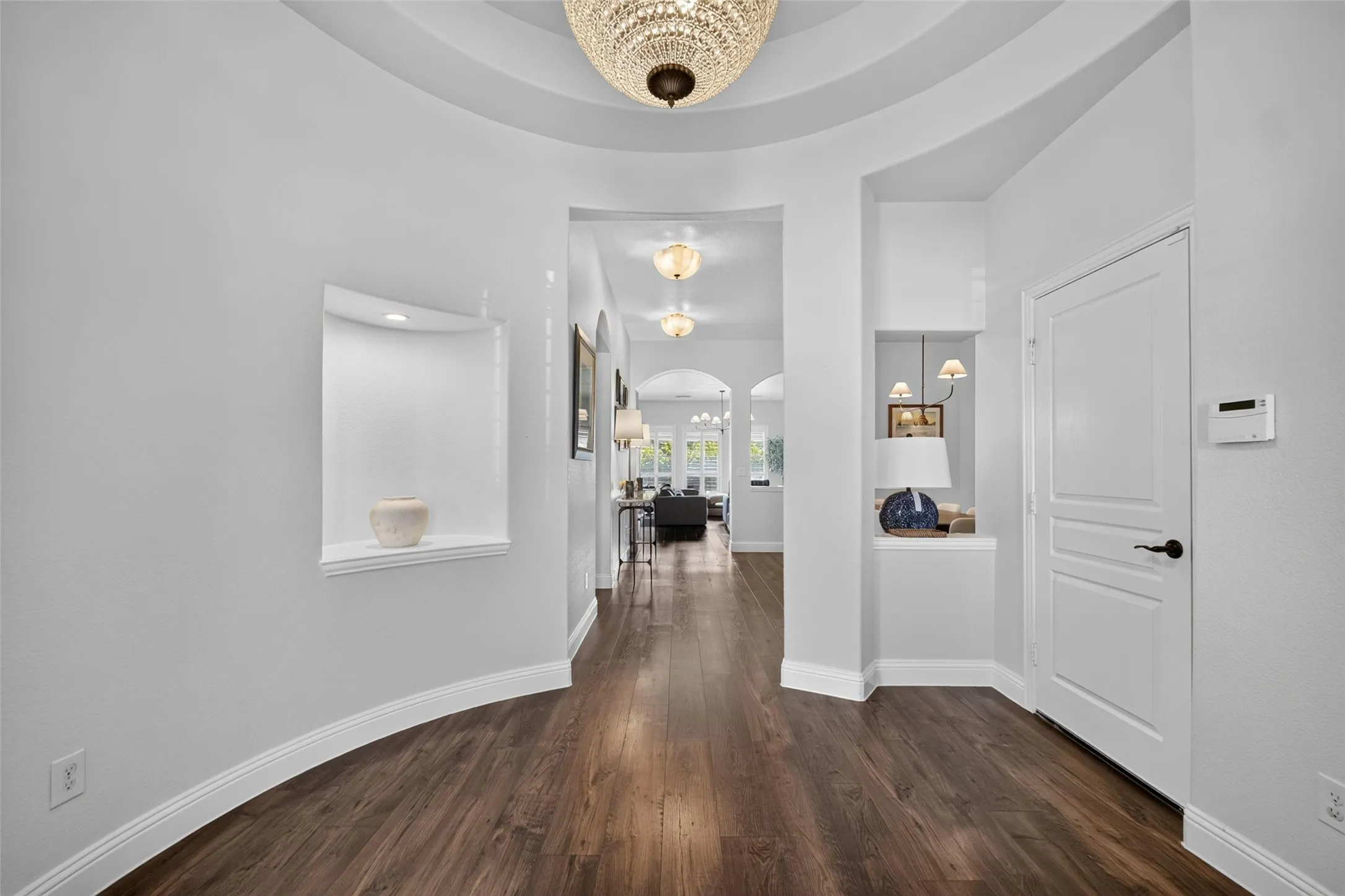 Foyer featuring wood-finish flooring, a tiered tray ceiling with a crystal chandelier, and two recessed wall niches
