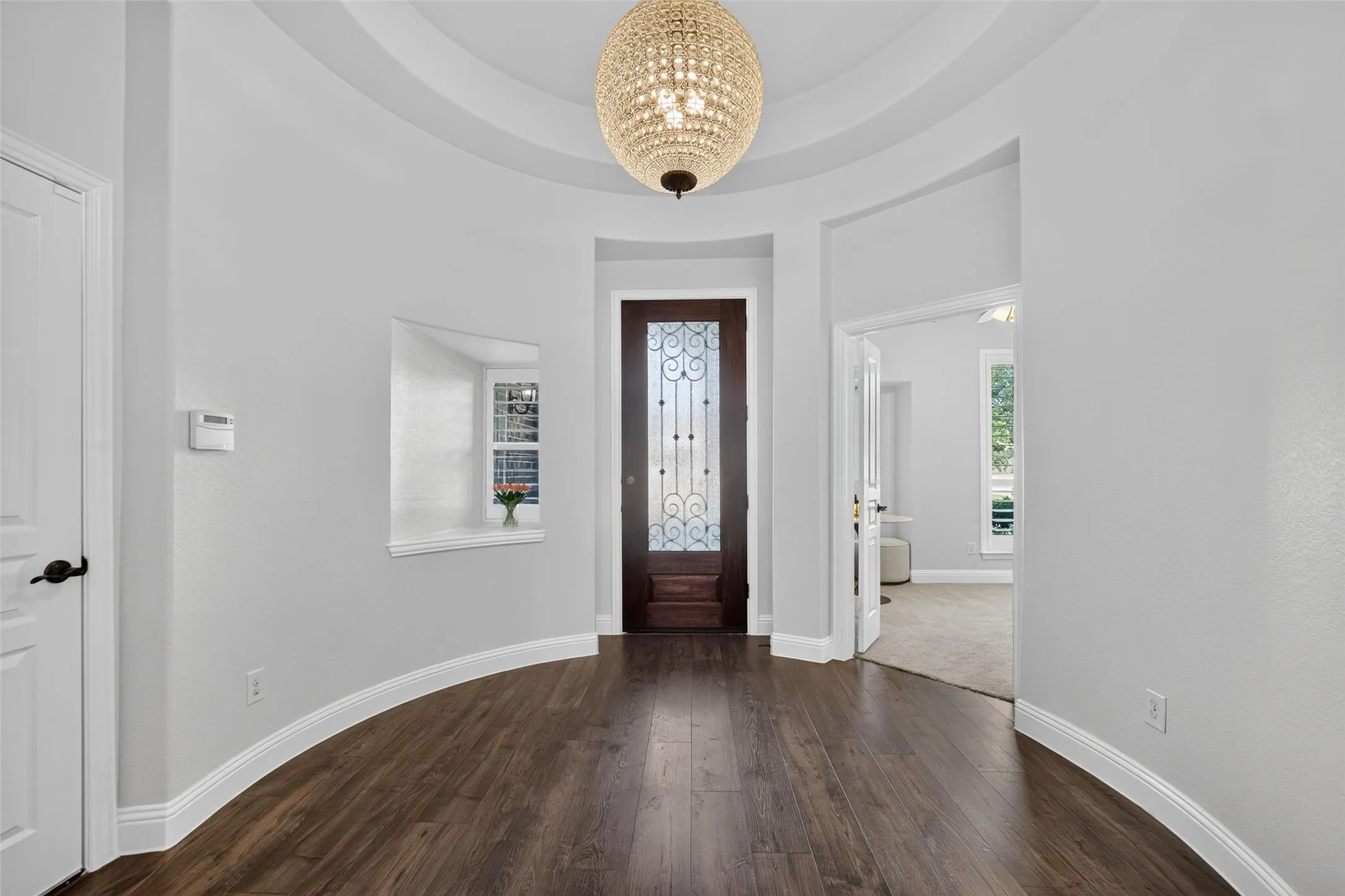 Rotunda entry featuring wood-finish flooring, a domed ceiling, a tiered crystal sphere chandelier, and a wood entry door with wrought iron detailing